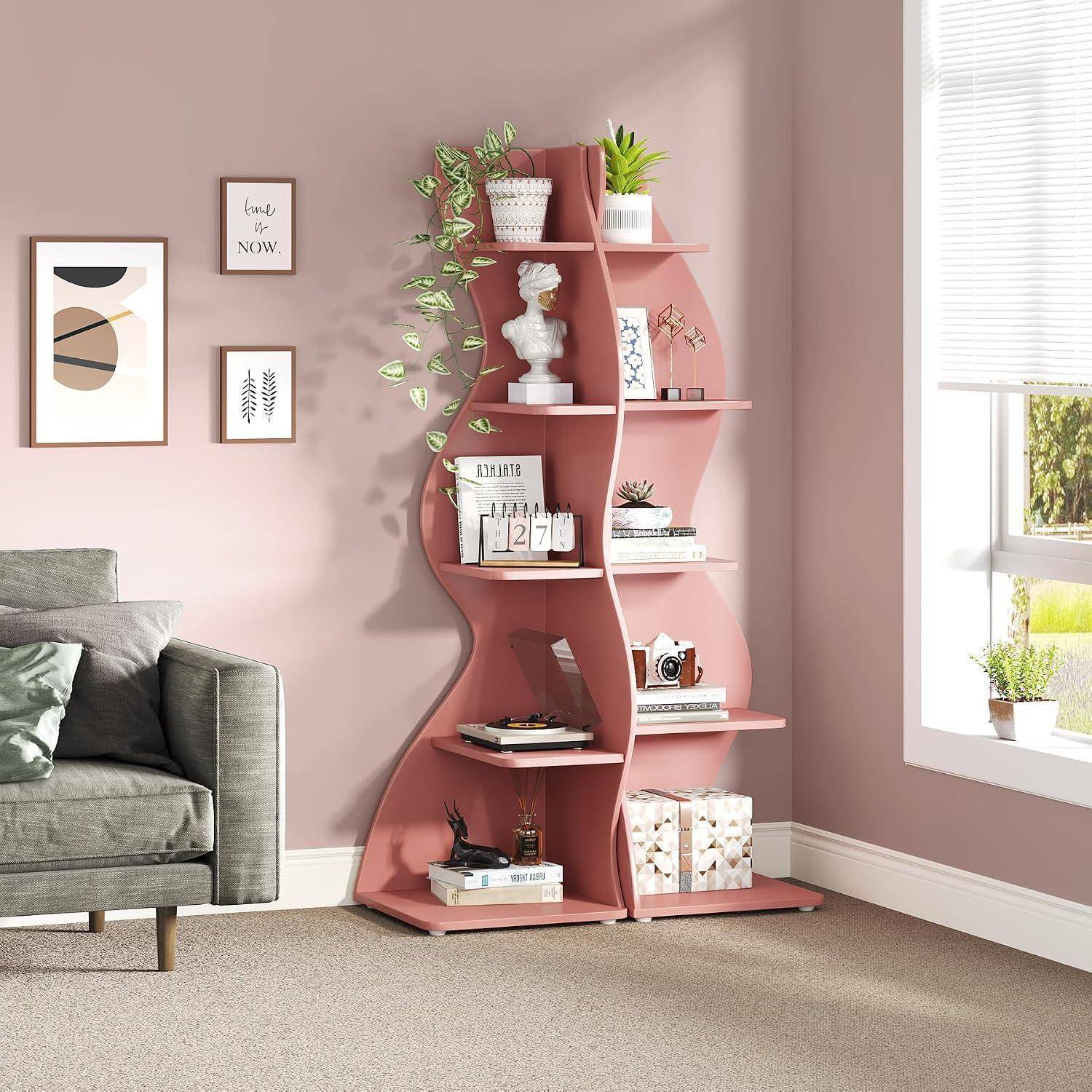Rosa, welliges Bücherregal mit Pflanzen, Büchern, Deko und einer Büste in einem Pastellwohnzimmer neben einem Sofa und hellem Fenster.