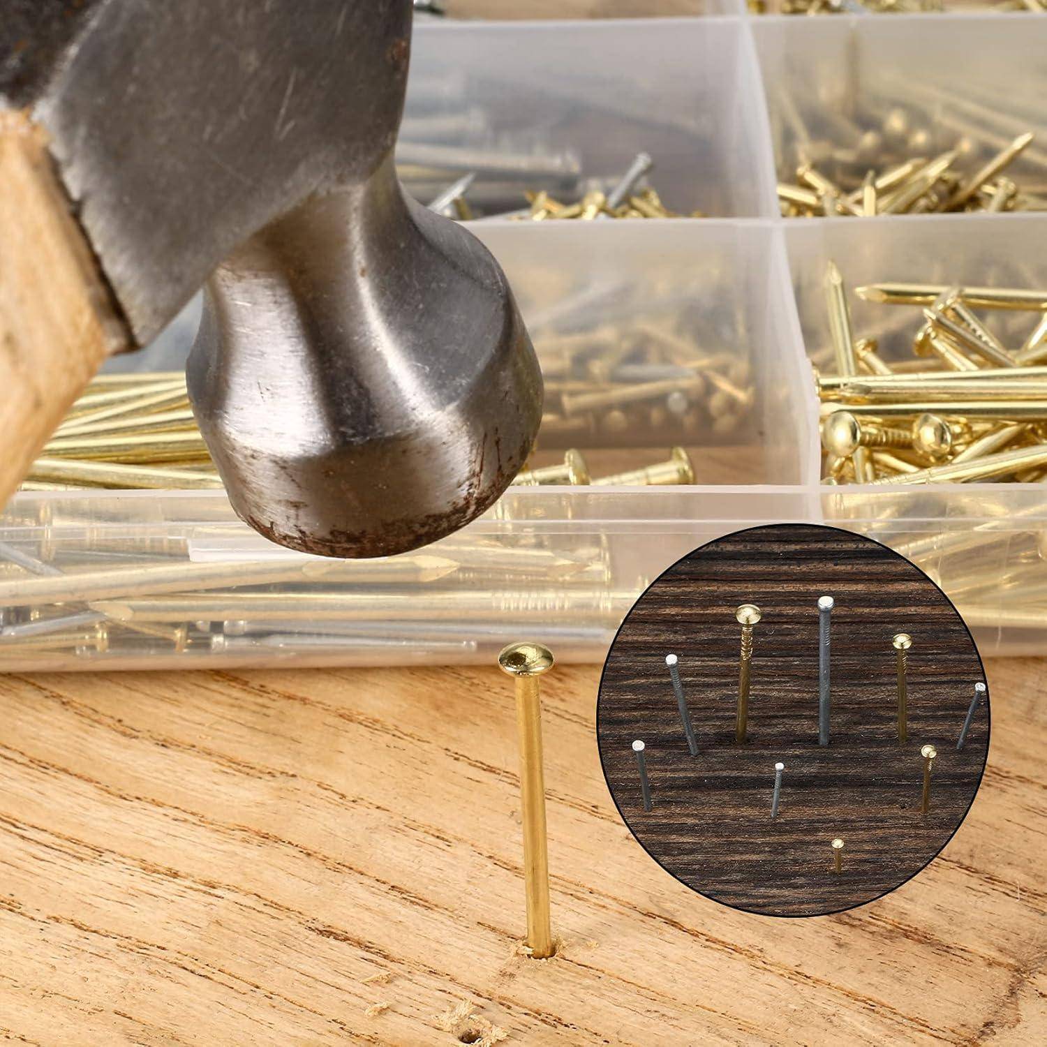 Hammer, der einen Messingnagel in Holz treibt, mit einem Teileorganizer mit verschiedenen Nägeln und Spitzennägeln im Hintergrund.