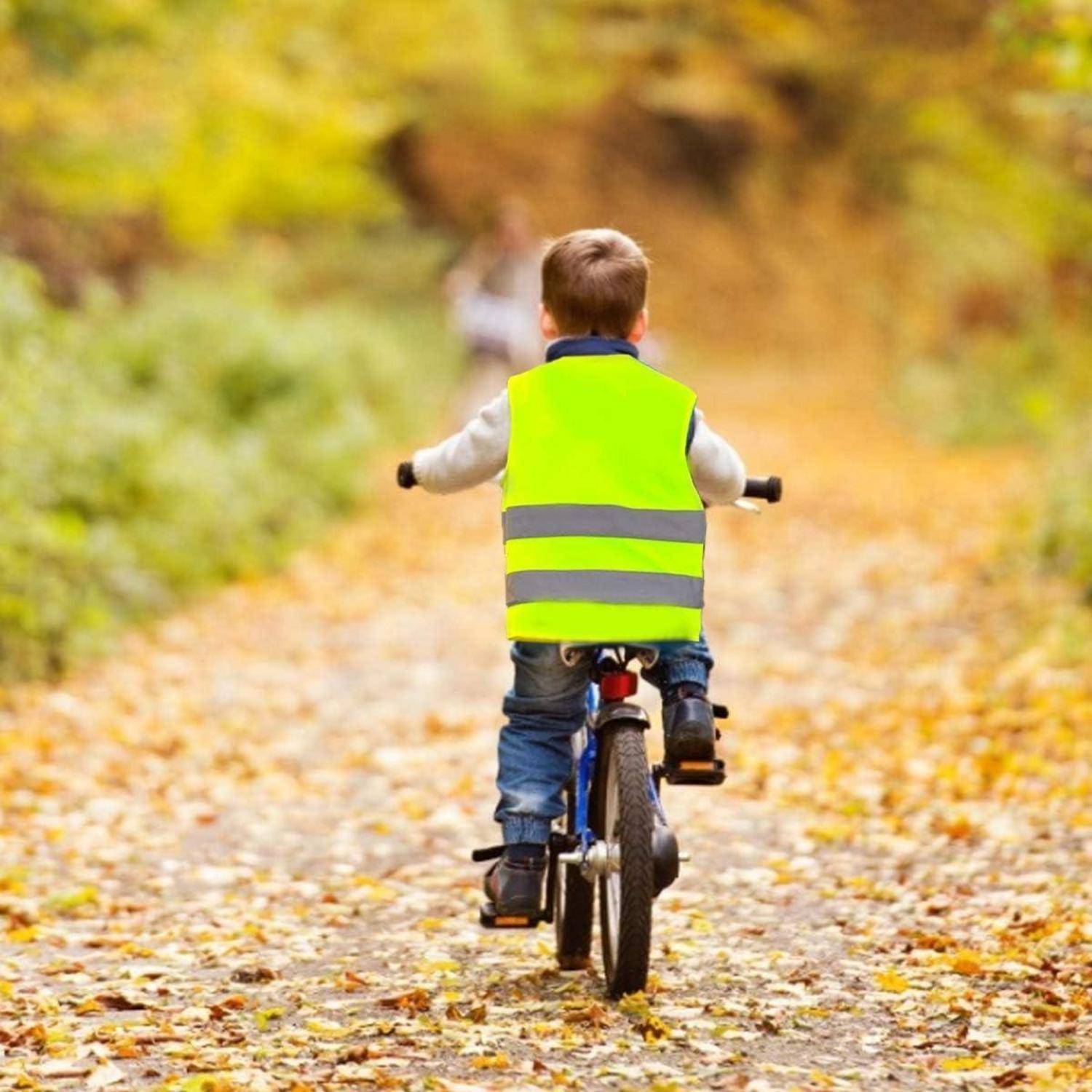 Ein Kind in einer leuchtend reflektierenden Weste fährt auf einem Fahrrad einen laubbedeckten Weg im Herbst hinunter.