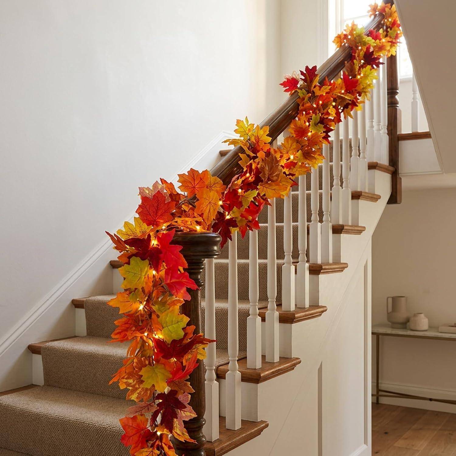 Treppe mit einer Girlande aus orangefarbenen, roten und gelben Herbstblättern, die entlang des Geländers in einem Wohnungsinneren angebracht ist.