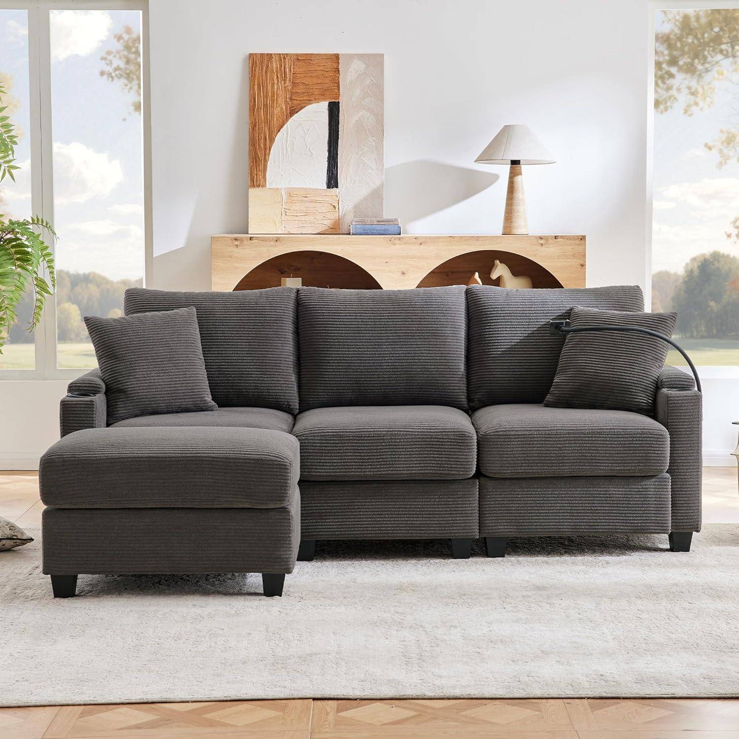 Dunkelgraues Ecksofa mit Chaiselongue, drei Kissen und gebogener Armlehne in einem hellen modernen Wohnzimmer mit Holzkonsole und Lampe.