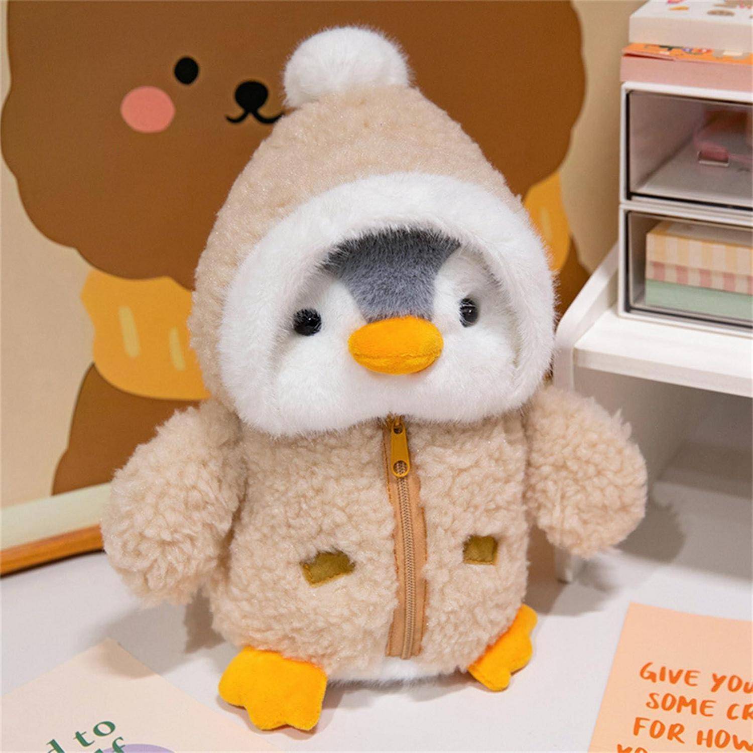 Weiches Pinguin-Spielzeug in einem beigen Kapuzenmantel mit Reißverschluss, auf einem Tisch neben einer Karte mit der Aufschrift „GIVE YOU SOME LOVE