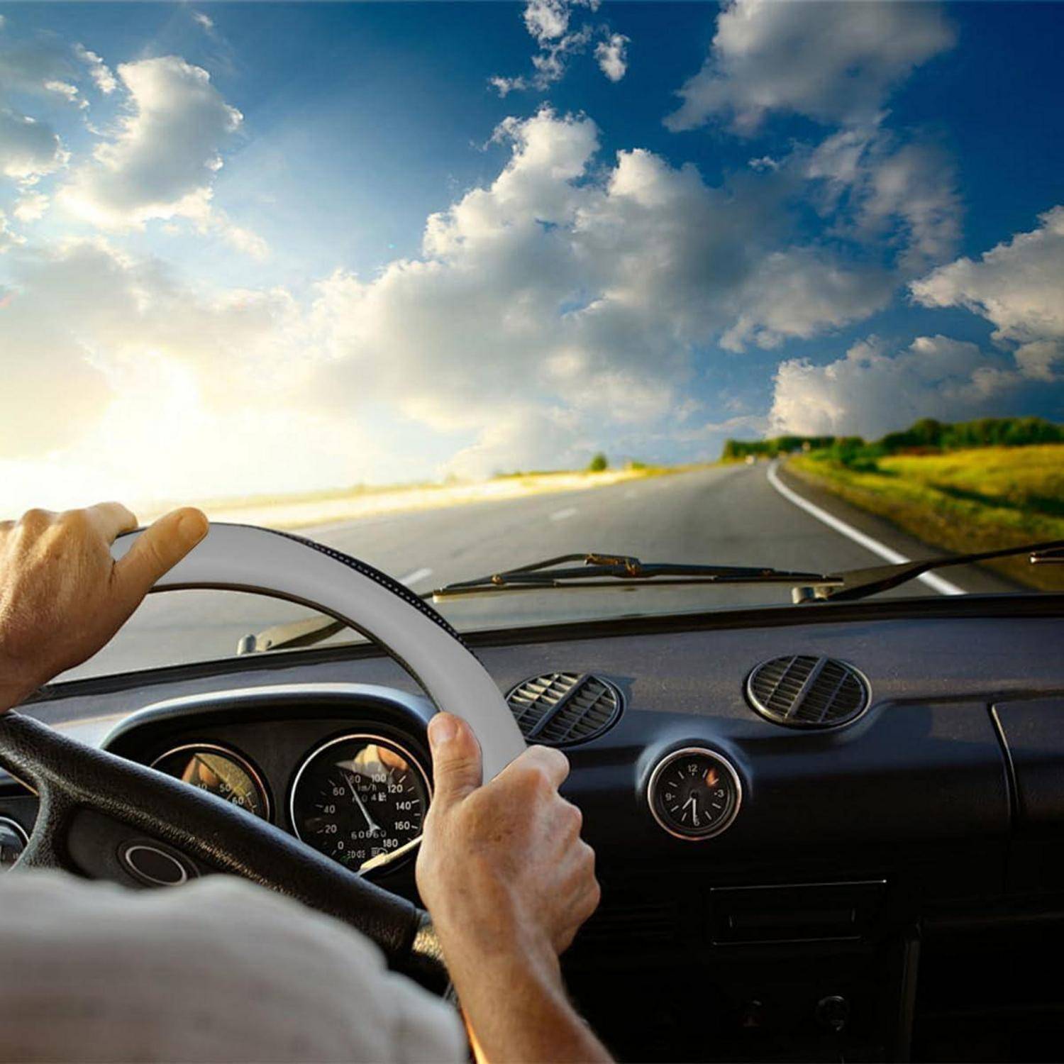 Blickwinkel des Fahrers aus dem Inneren eines Autos auf einer kurvigen Straße, Hände am Lenkrad unter einem hellen Himmel mit Wolken.