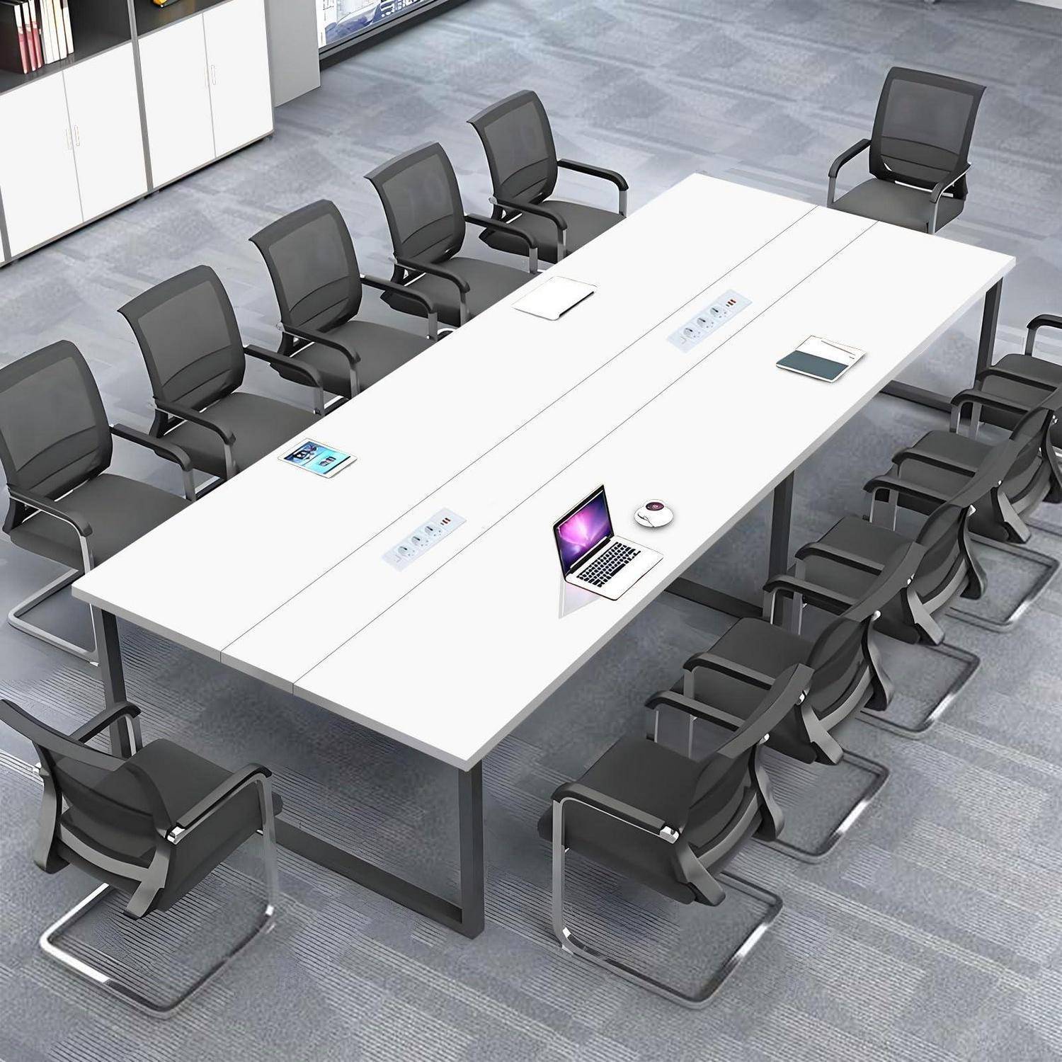 Leerer moderner Konferenzraum mit einem langen weißen Tisch, umgeben von schwarzen Stühlen; ein Laptop und kleine Geräte liegen auf der Tischplatte.