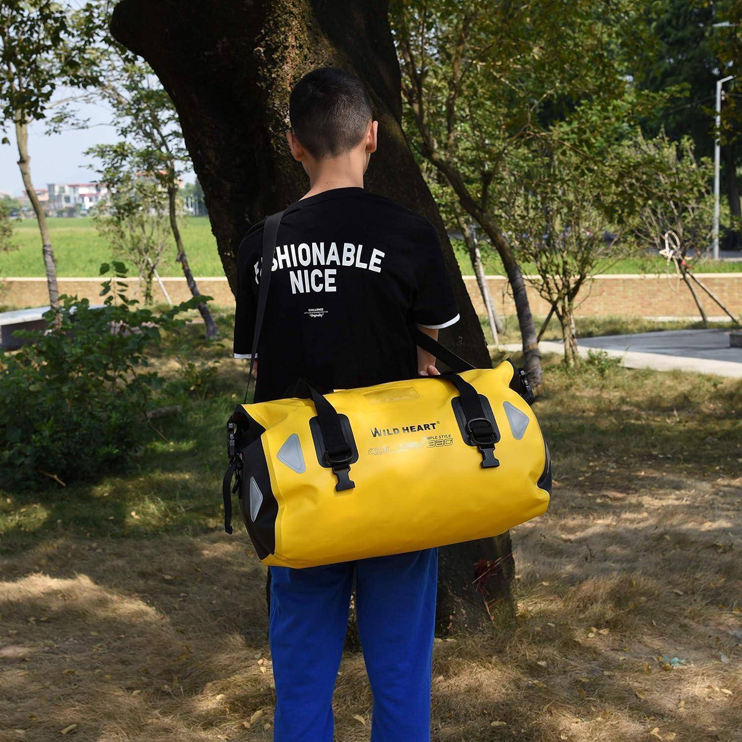 Eine Person steht draußen neben einem Baum mit einer großen gelben Reisetasche über der Schulter gehängt.