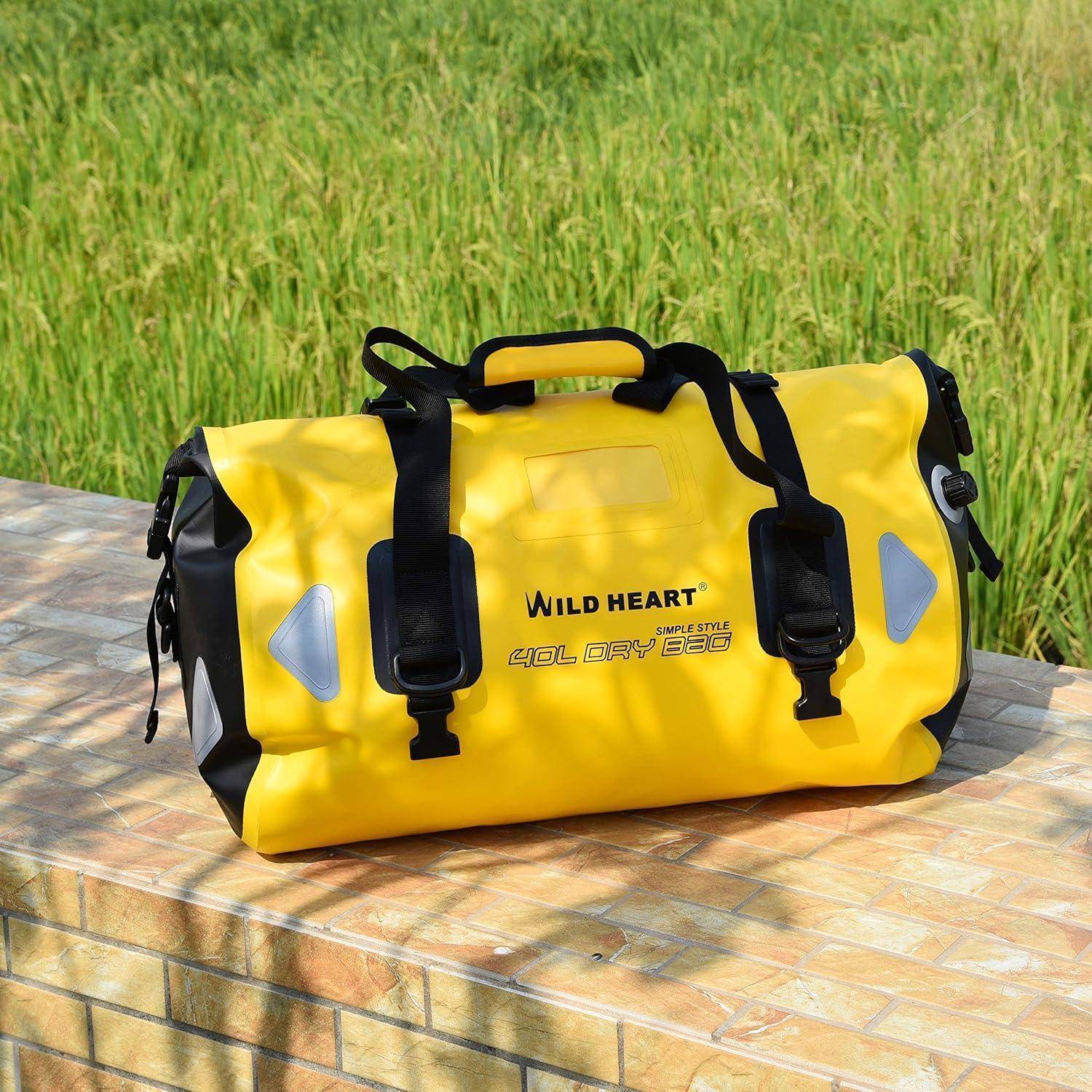 Gelbe wasserdichte Sporttasche mit schwarzen Riemen, gekennzeichnet mit 'WILD HEART', sitzt auf einer gefliesten Bank im Freien vor Gras.