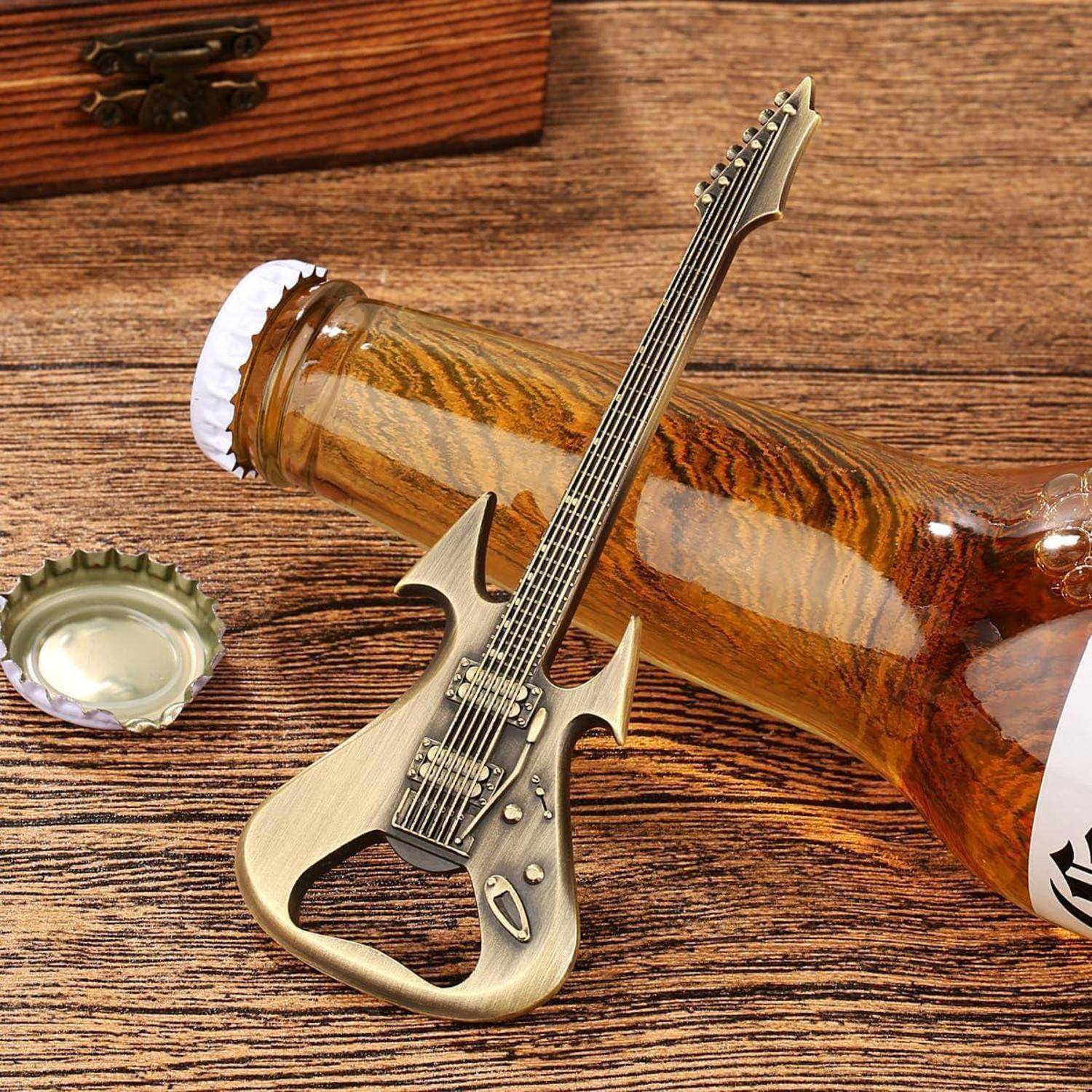 Miniatur-Elektrogitarren-förmiger Flaschenöffner neben einer Kappe aus bernsteinfarbenem Glas auf einer Holzoberfläche.