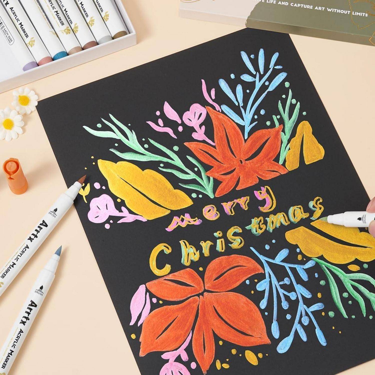 Handgezeichnetes Weihnachtskarten-Design auf schwarzem Papier mit bunten Blumen, Blättern und dem Text „Frohe Weihnachten