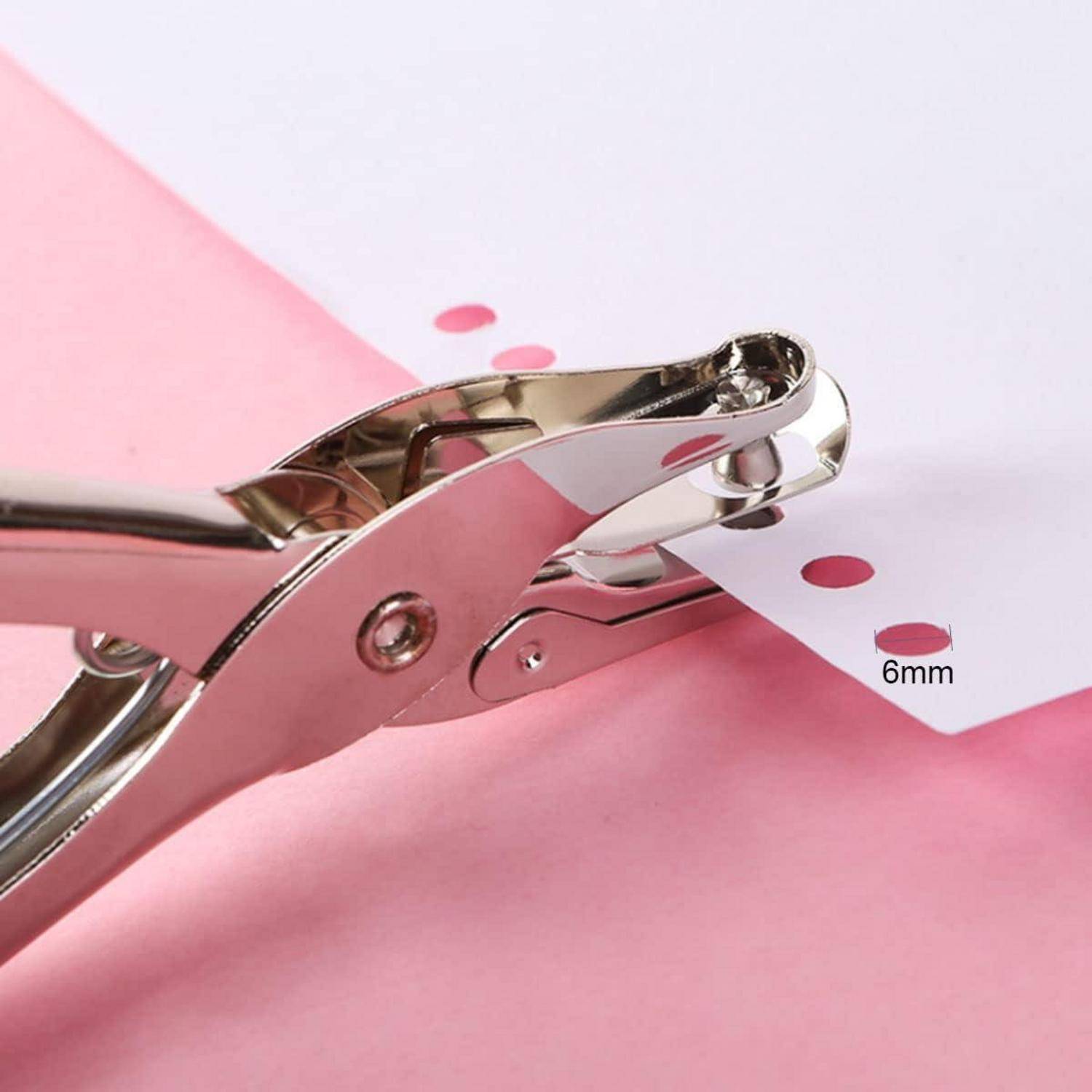 Nahaufnahme eines Lochers, der sechs 6-mm-Löcher entlang der Kante eines weißen Blattes auf rosa Papier stanzt.