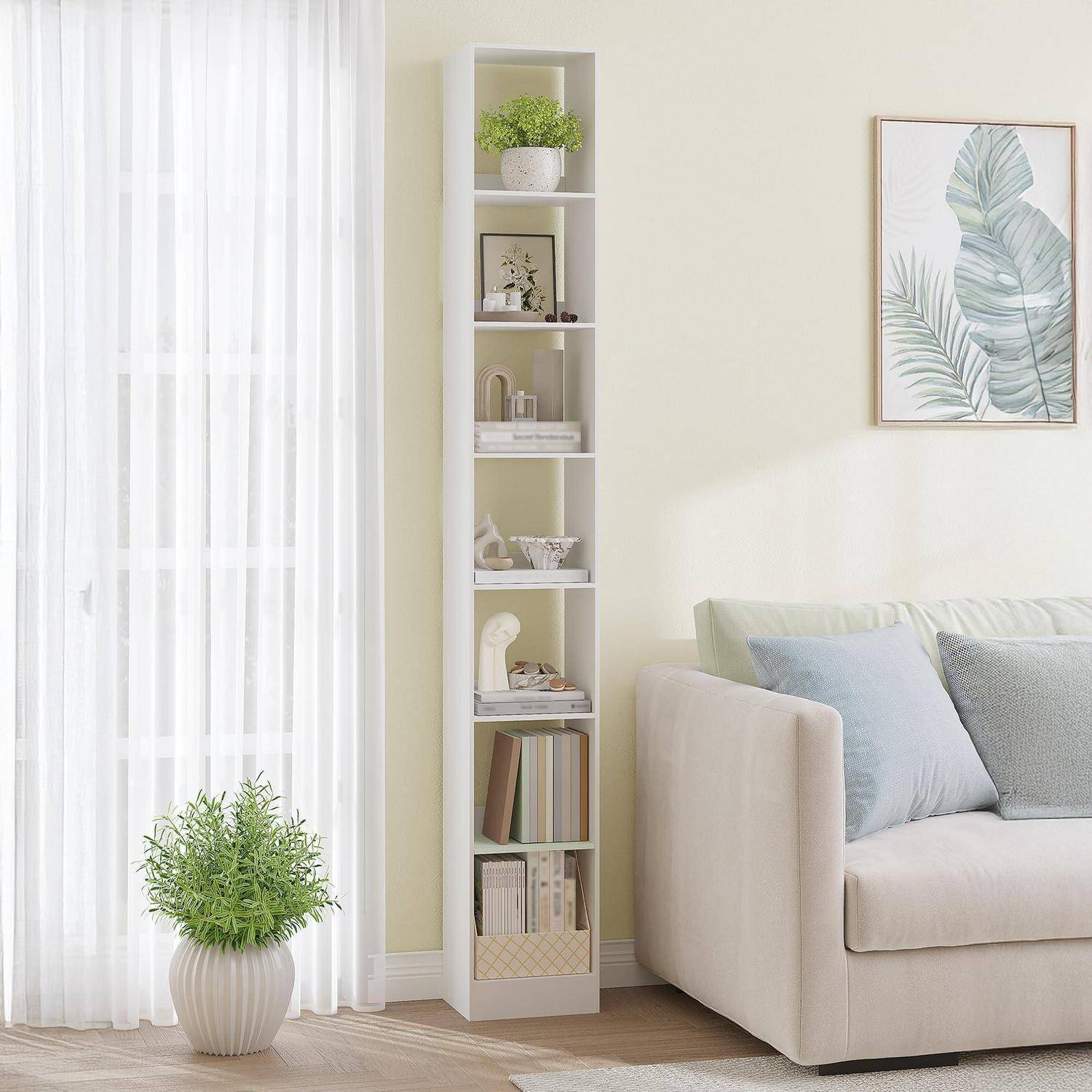 Helles Wohnzimmer mit beigem Sofa, hohem weißem Regal, Topfpflanze, transparenten Vorhängen und gerahmtem Blattmotiv-Kunstwerk an der Wand.