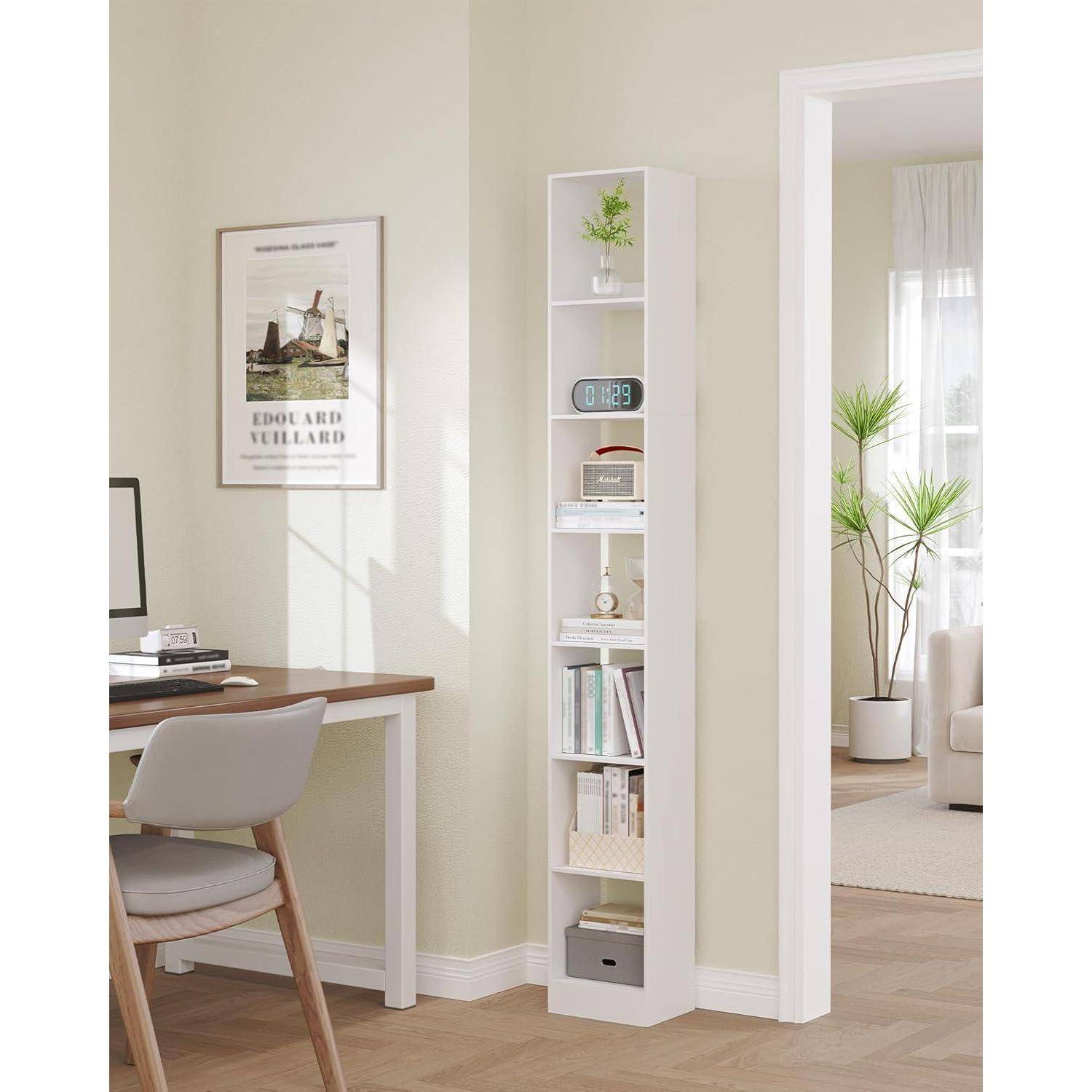 Helles Homeoffice mit Schreibtisch und Stuhl neben einem schmalen weißen Regal, das Deko, Bücher und eine digitale Uhr enthält, das sich in ein sonniges Wohnzimmer öffnet.