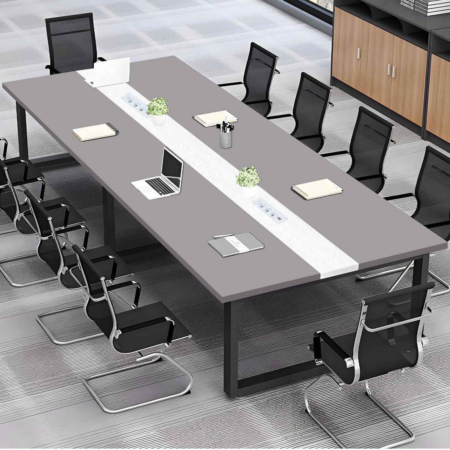 Moderner Konferenzraum mit einem langen rechteckigen Tisch, mehreren schwarzen Stühlen, Laptops, Notizbüchern und kleinen Pflanzen rund um eine zentrale Steckdosenleiste.