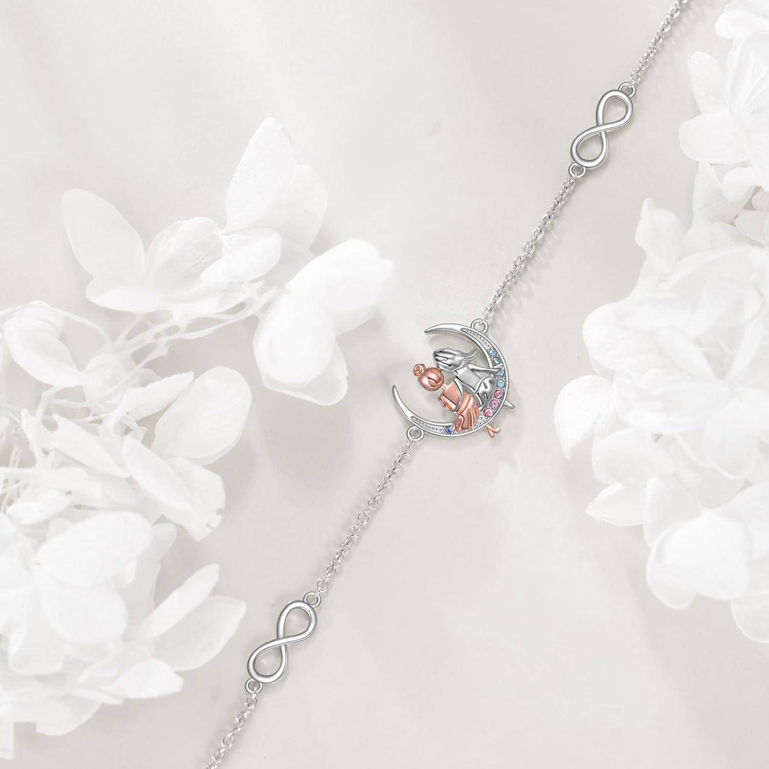 Silbernes Armband mit Unendlichkeitsgliedern und einem Mondsichel-Charm mit einer kleinen rosa-silbernen Figur, gezeigt auf hellem Hintergrund mit weißen Blüten.
