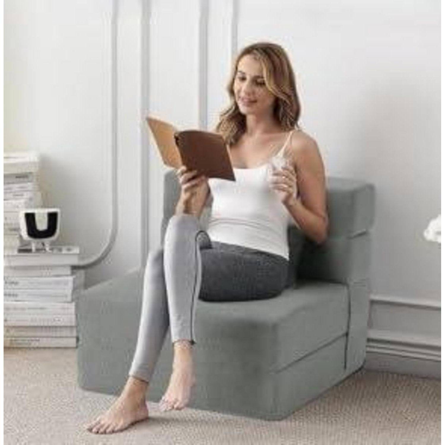 Eine Frau sitzt in einem grauen Stuhl und liest ein Buch in einem hellen, minimalistischen Raum.