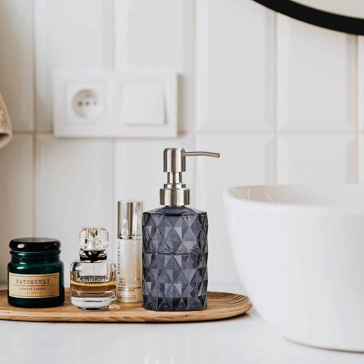 Badezimmerarbeitsplatte mit einem Seifenspender, Parfumflaschen und einer Kerze auf einem Holztablett neben einem weißen Waschbecken und einer gefliesten Wand.