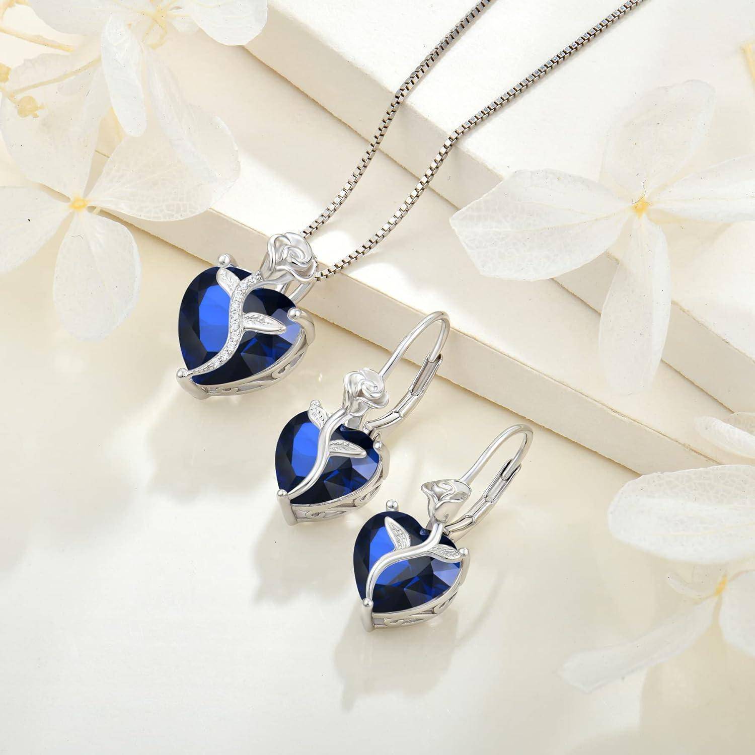Silberne herzförmige blaue Edelsteinkette und passende Ohrringe auf hellem dekorativem Hintergrund präsentiert.