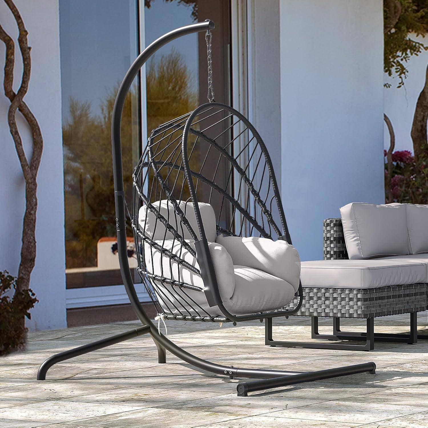 Outdoor-Terrasse mit einem hängenden Eiersessel und einem gepolsterten Rattansofa neben einer Glastür.