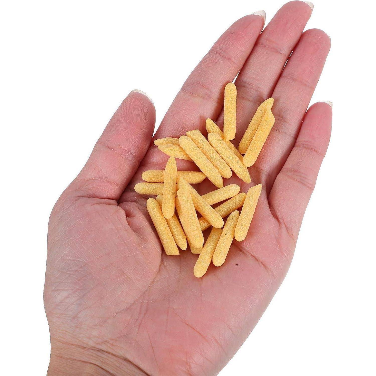 Eine Hand, die einen kleinen Haufen gelber Holzstäbchen auf weißem Hintergrund hält.