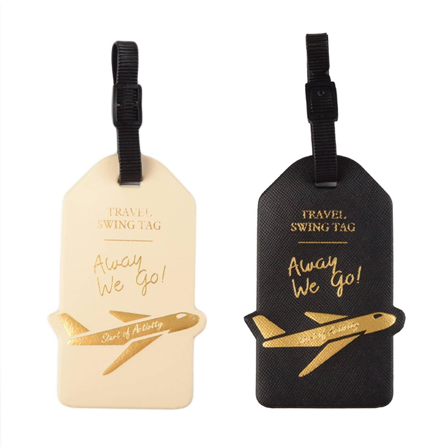 Zwei Reise-Kofferanhänger im Swing-Design, einer in Creme und einer in Schwarz, jeweils mit einem schwarzen Riemen und einer goldenen Flugzeuggrafik mit der Aufschrift „Away we go!