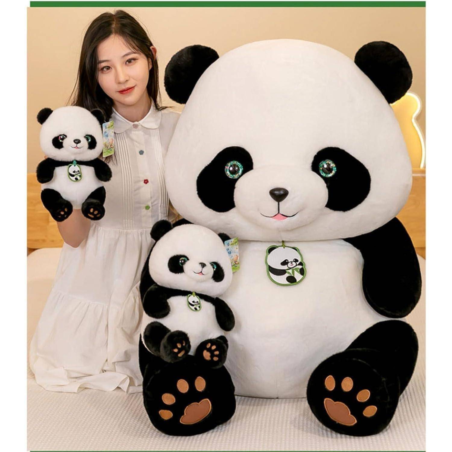 Eine Frau in einem weißen Kleid posiert mit zwei Plüsch-Pandas, einem großen und einem kleinen, in einer Studioumgebung.