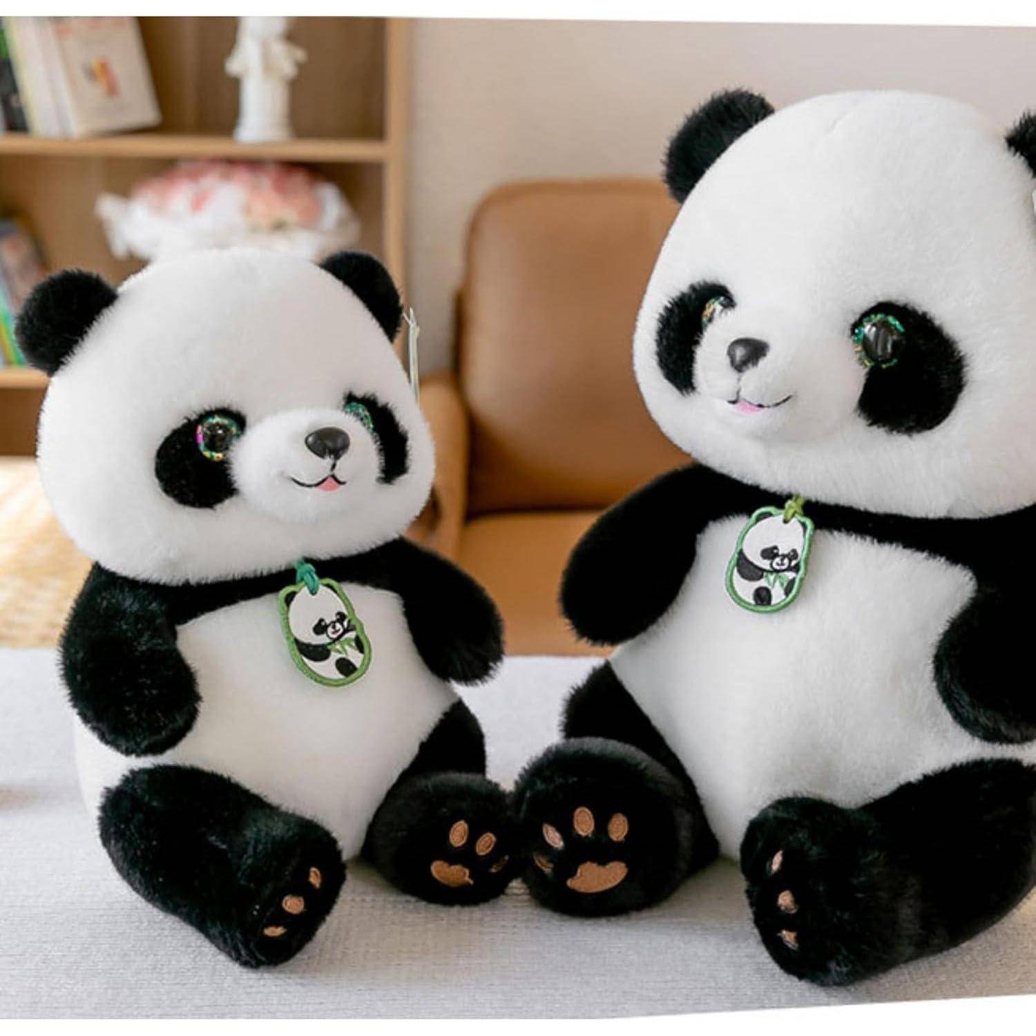 Zwei weiche Panda-Spielzeuge sitzen zusammen auf einem Bett oder einer Couch, ein kleineres und ein größeres, jedes mit einem grünen Panda-Etikett.