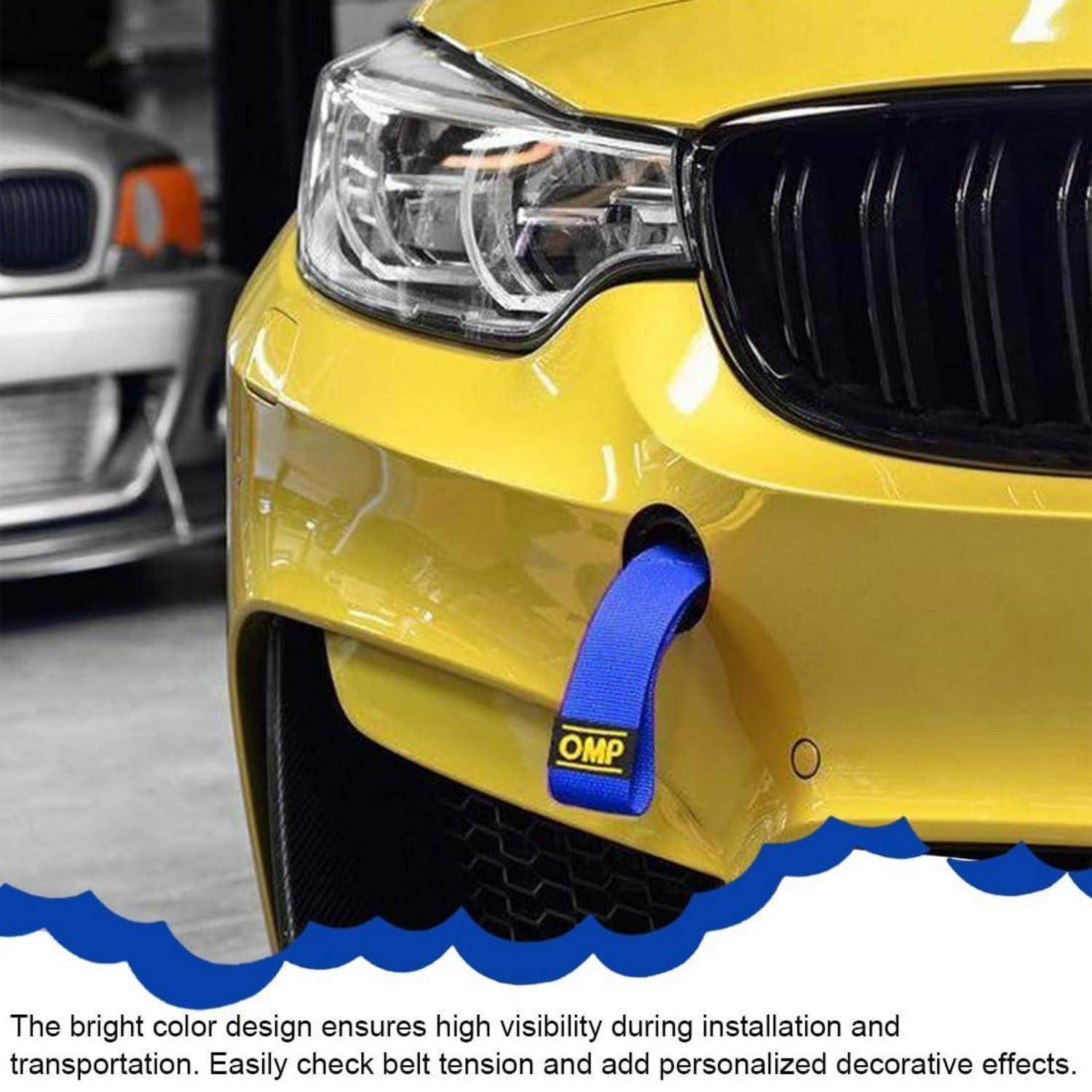 Nahaufnahme der vorderen Stoßstange eines gelben Autos mit einem blauen OMP-Abschleppgurt, der neben einem silbernen Auto geparkt ist; die Bildunterschrift hebt die hohe Sichtbarkeit während der Installation und Reparatur hervor.