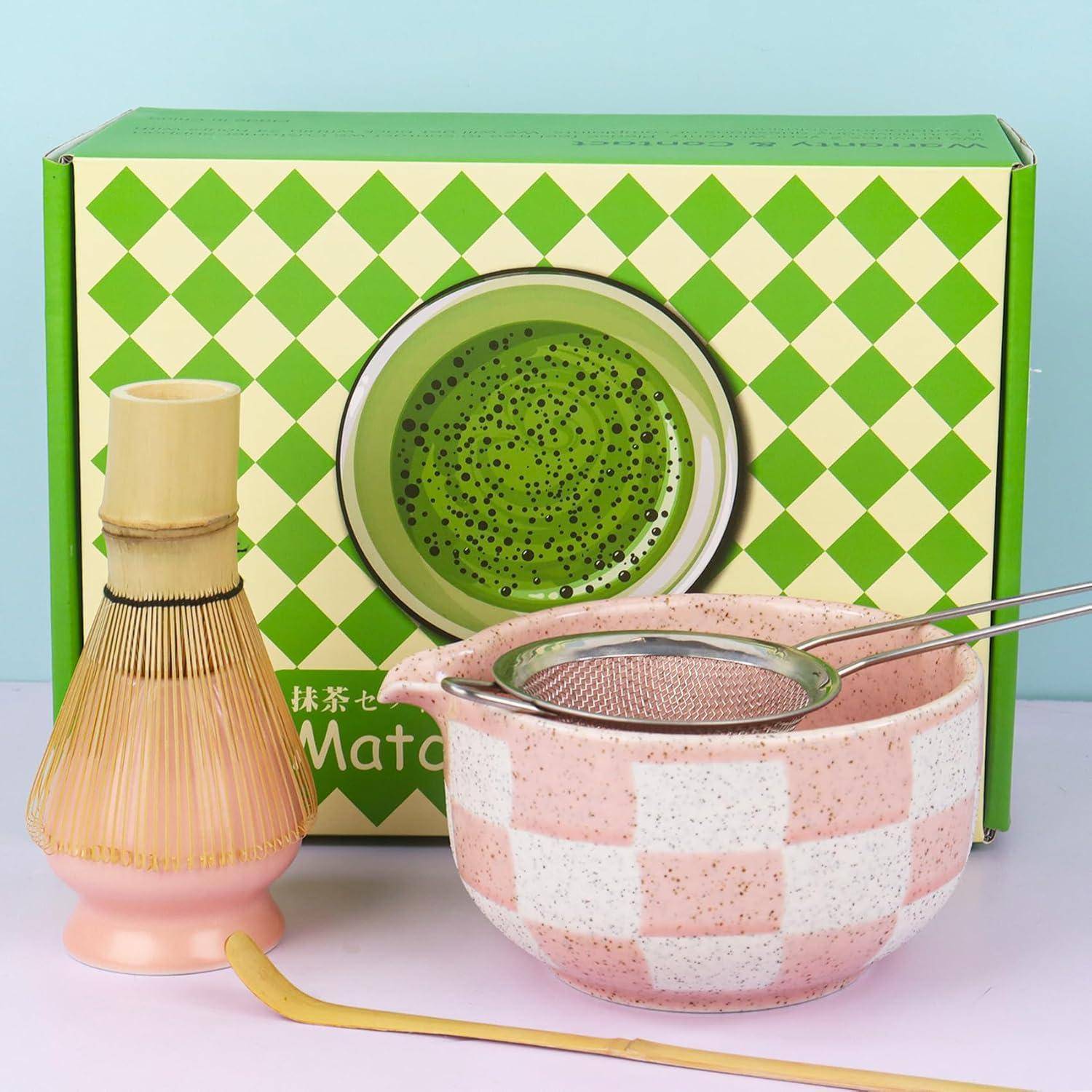 Matcha-Tee-Set mit Bamboosbesen, rosa Chasen-Halter und Schale mit Sieb vor einer grünen karierten Schachtel.