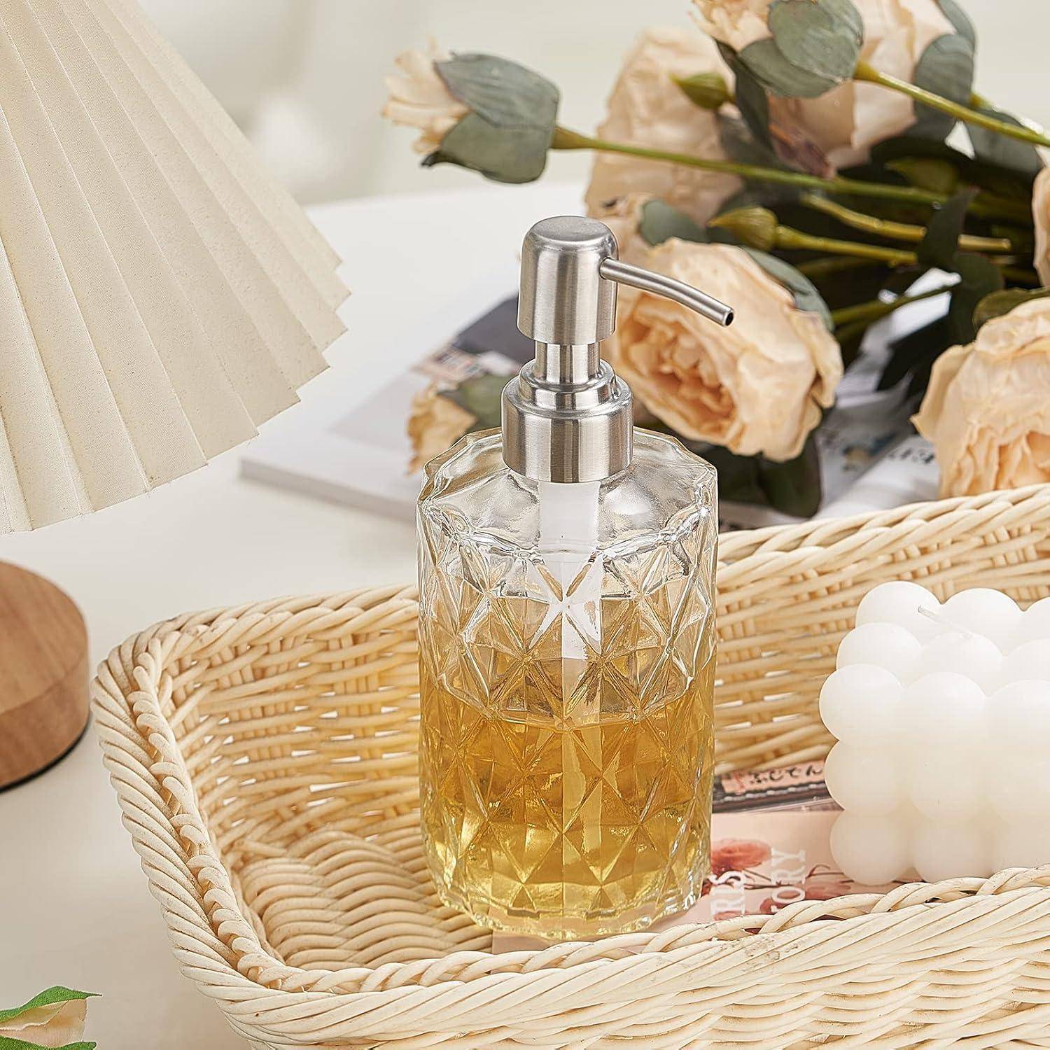 Glassseifenspender mit bernsteinfarbener Flüssigkeit in einem geflochtenen Tablett, stilisiert mit Blumen, einer Lampe und einer dekorativen Kerze auf einem Tisch.