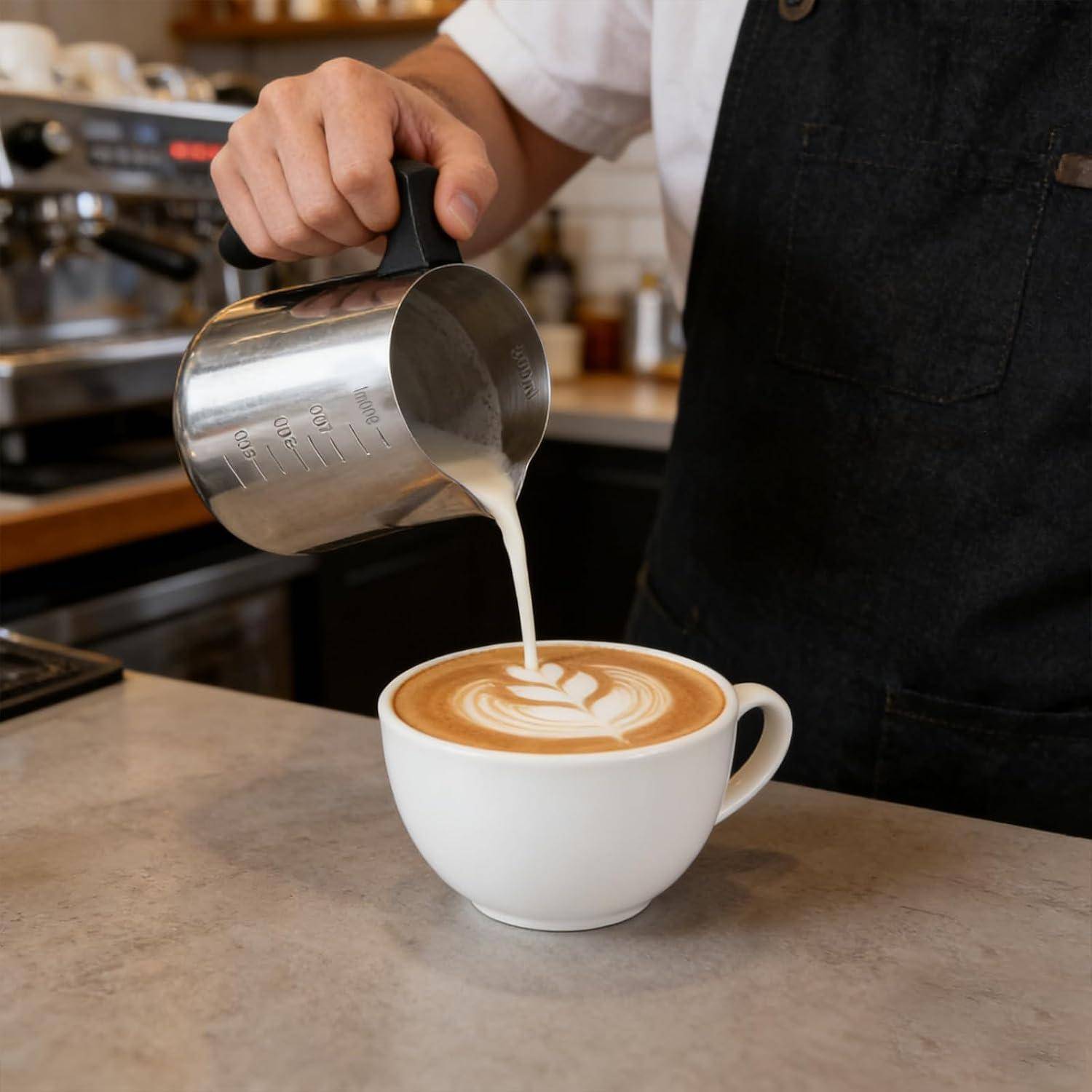 Barista gießt aufgeschäumte Milch in eine Tasse Latte und kreiert dabei Latte Art auf der Kaffeeoberfläche.