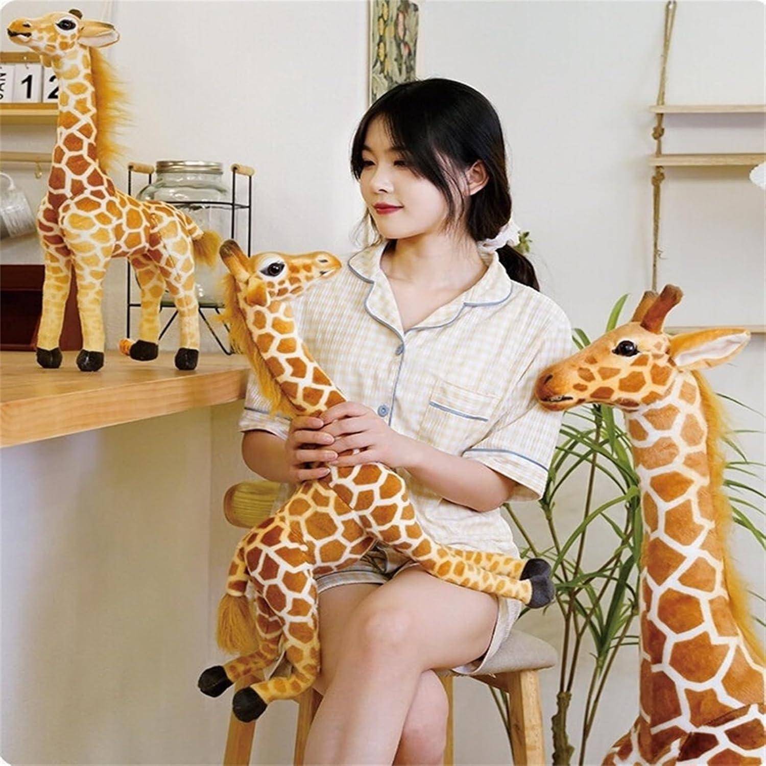 Frau sitzt im Innenraum und hält ein weiches Giraffenspielzeug in der Hand, umgeben von mehreren Giraffen-Plüschtieren auf einem Regal und auf dem Boden.