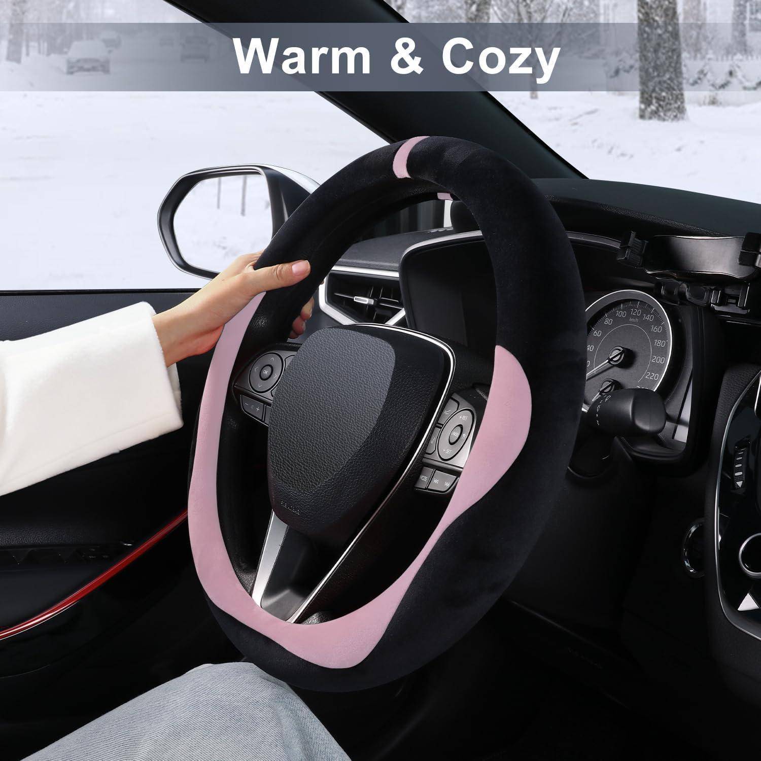 Hand hält eine rosa-schwarze Plüsch-Lenkradabdeckung in einem Autoinnenraum, mit dem Text "Warm & Cozy"", der Winterkomfort suggeriert.