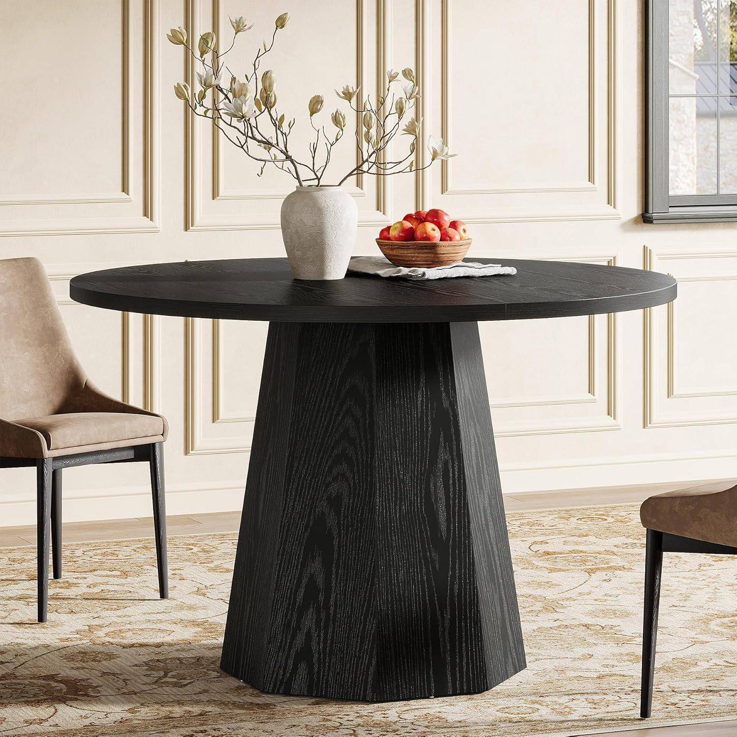 Schwarzer runder Säulentisch mit Vase und Schüssel mit Äpfeln in einem hellen, eleganten Esszimmer mit gepolsterten Stühlen.