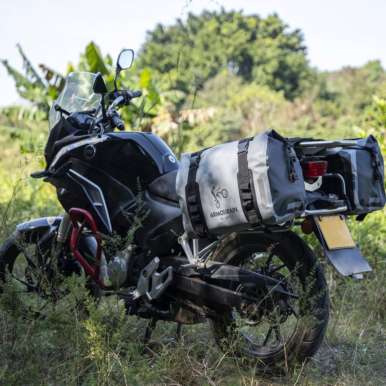 Schwarzes Abenteuermotorrad geparkt im Gras mit Seitenkoffern und einer grauen Satteltasche, im Freien in einer grünen ländlichen Gegend.