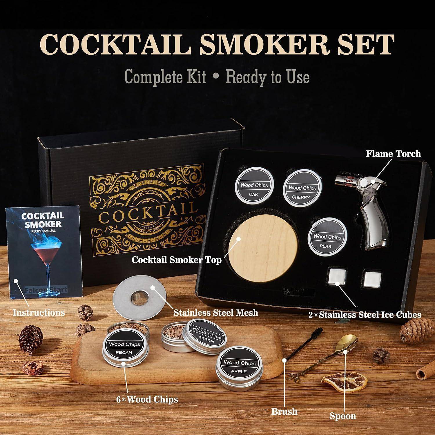 Cocktail-Räucher-Set auf einem Holztisch, zeigt eine Schachtel, einen Brenner, Holzchips, Stahlgitter, Eiswürfel, eine Bürste, einen Löffel und Anleitung zum Zubereiten von geräucherten Cocktails.