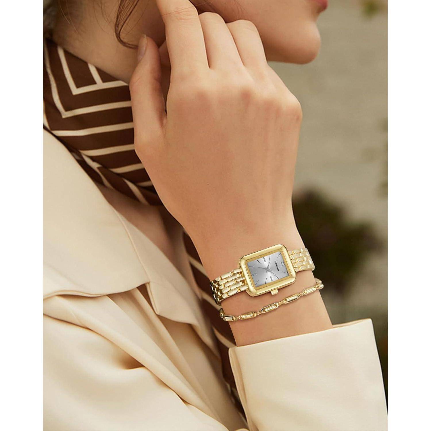 Nahaufnahme einer Frau, die eine goldene Armbanduhr und ein Kettenarmband zu einem cremefarbenen Outfit und einem gestreiften Schal trägt.
