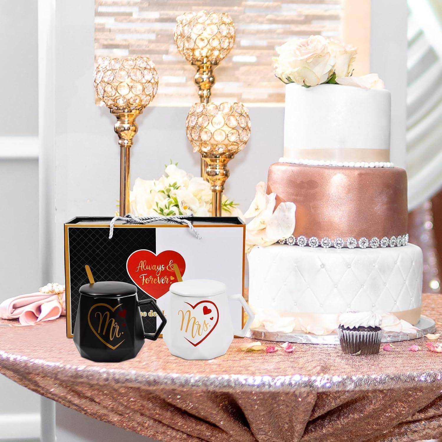 Hochzeitstortenpräsentation mit „Mr."- und „Mrs.""-Bechern, Blumendekoration und goldenen Kerzenhaltern auf einem Roségold-Tisch.