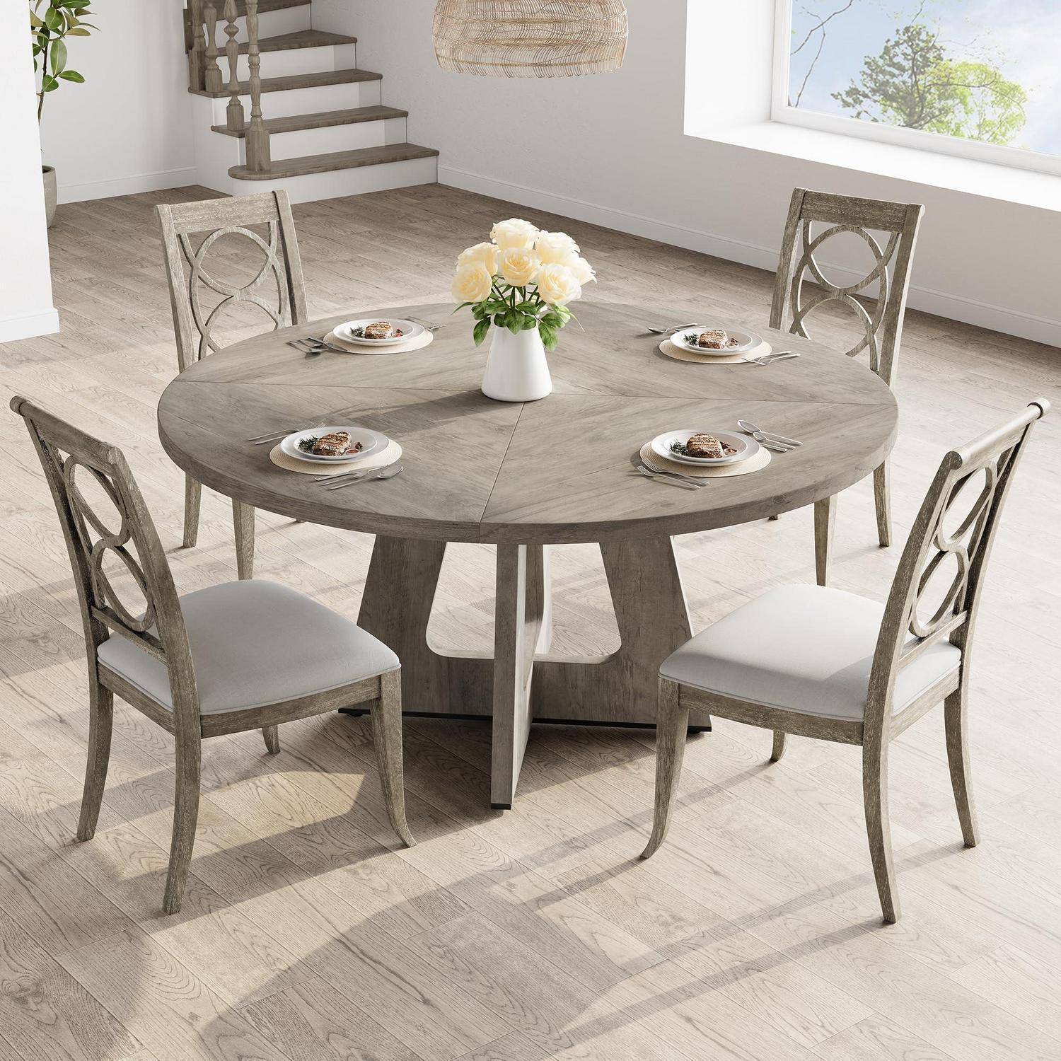 Runder Holzesstisch mit vier gepolsterten Stühlen in einem hellen modernen Zimmer, eingedeckt mit Tellern und einer Blumenvase.