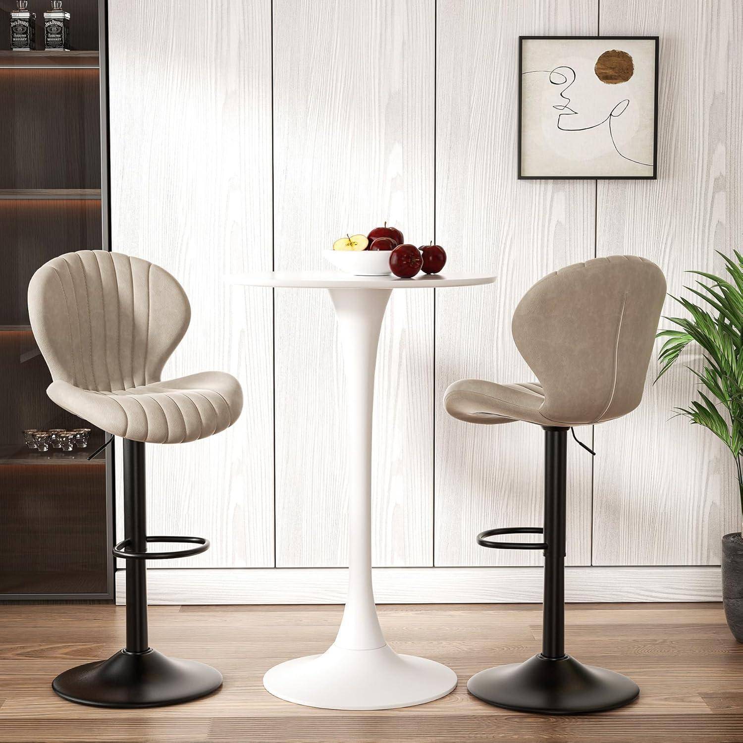 Zwei beige gepolsterte Barhocker flankieren einen kleinen weißen Säulentisch mit Obst in einem modernen Zimmer mit Wandkunst und einer Pflanze.
