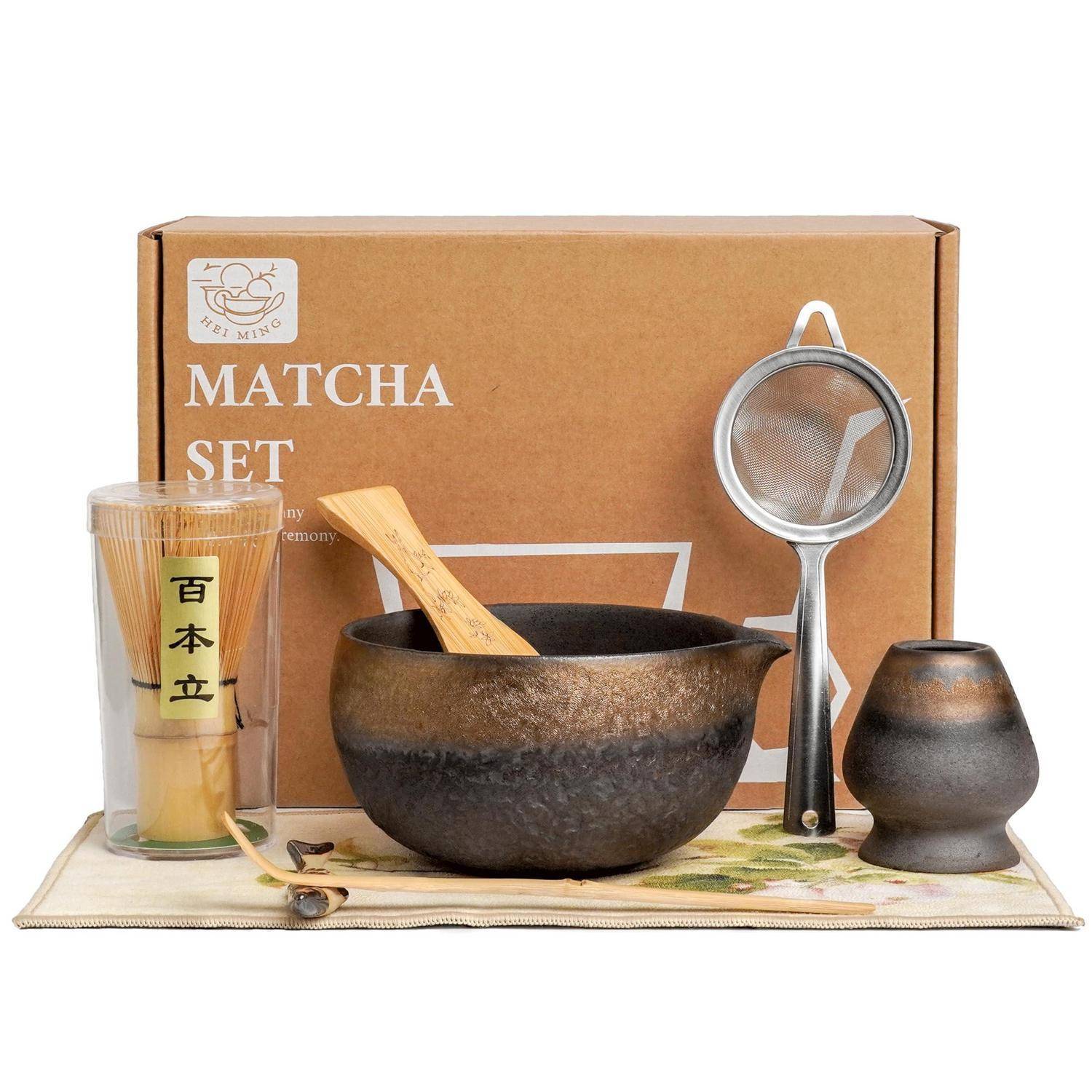 Matcha-Set mit Schale, Bamboosbesen, Löffel, Sieb, Tasse und Tuch, das vor einer braunen Schachtel mit der Aufschrift 