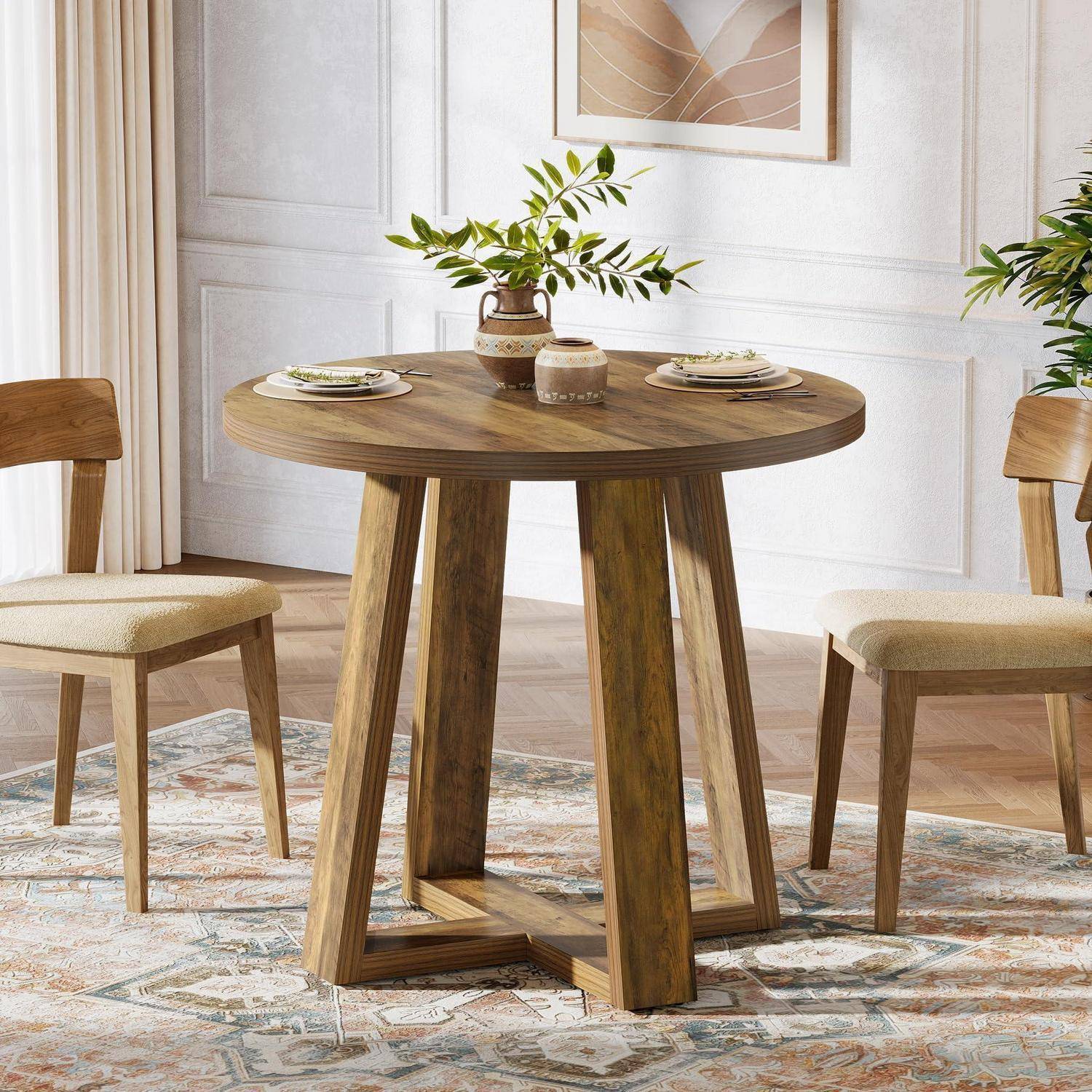 Rundes Holz-Esstischset für zwei Personen in einem hellen, modernen Esszimmer mit gepolsterten Stühlen, Gedeck und einer Vase mit Grünpflanzen.
