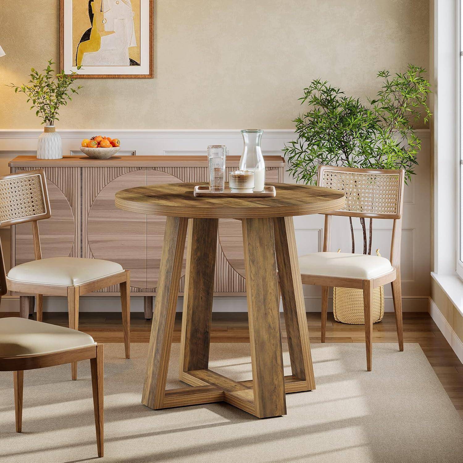 Eine helle Essecke mit einem runden Holztisch, vier geflochtenen Stühlen, Topfpflanzen und einem Sideboard an einer neutralen Wand.