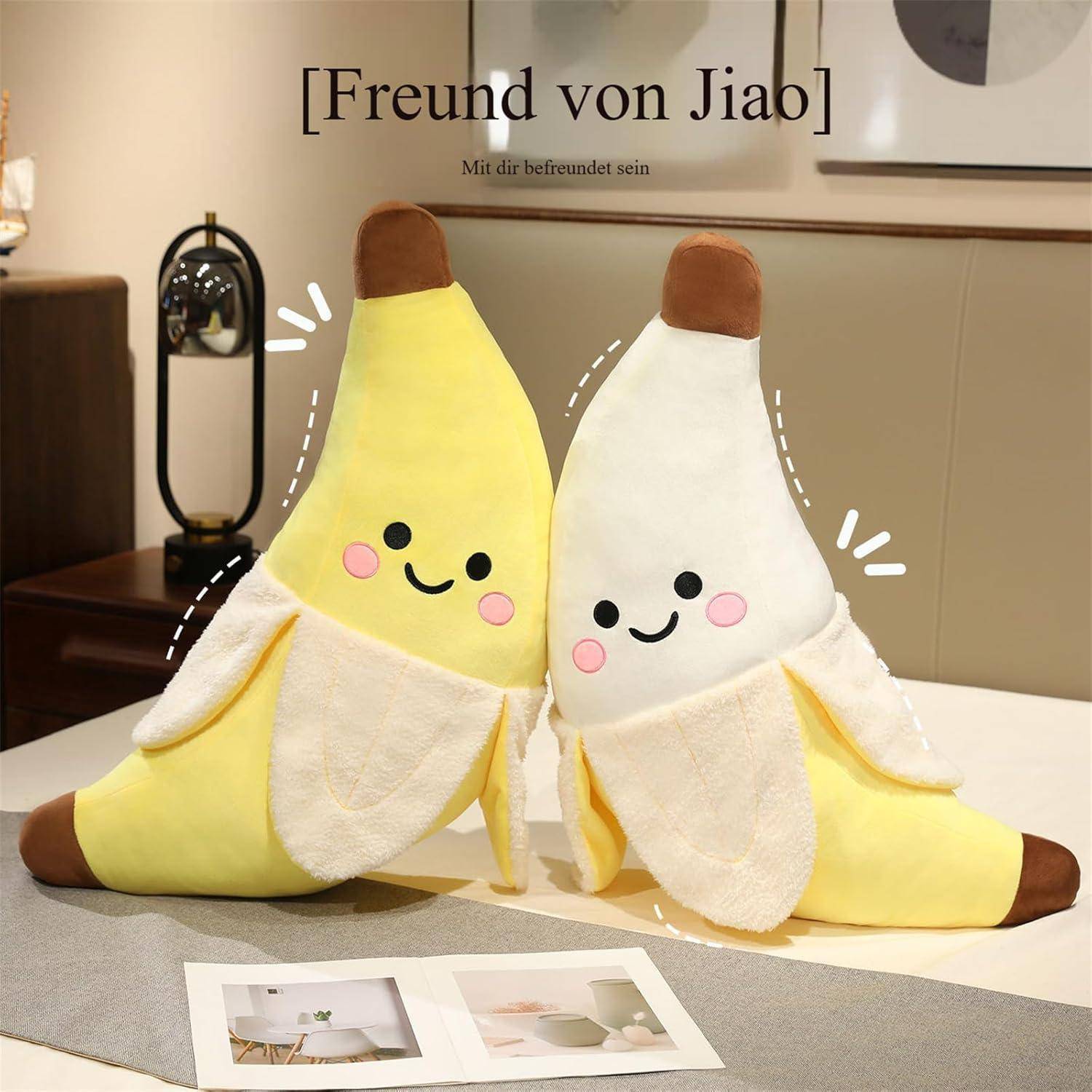 Zwei süße banannenförmige Plüschkissen sitzen auf einem Bett, eines gelb und eines weiß geschält, jedes mit einem lächelnden Gesicht.