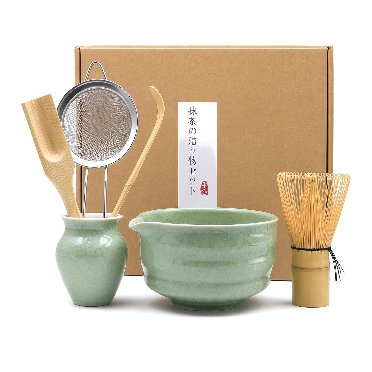 Matcha-Tezeremonie-Set mit einer grünen Schale, Schneebesen, Löffel, Sieb und vasenähnlichem Behälter vor einer beschrifteten Schachtel.