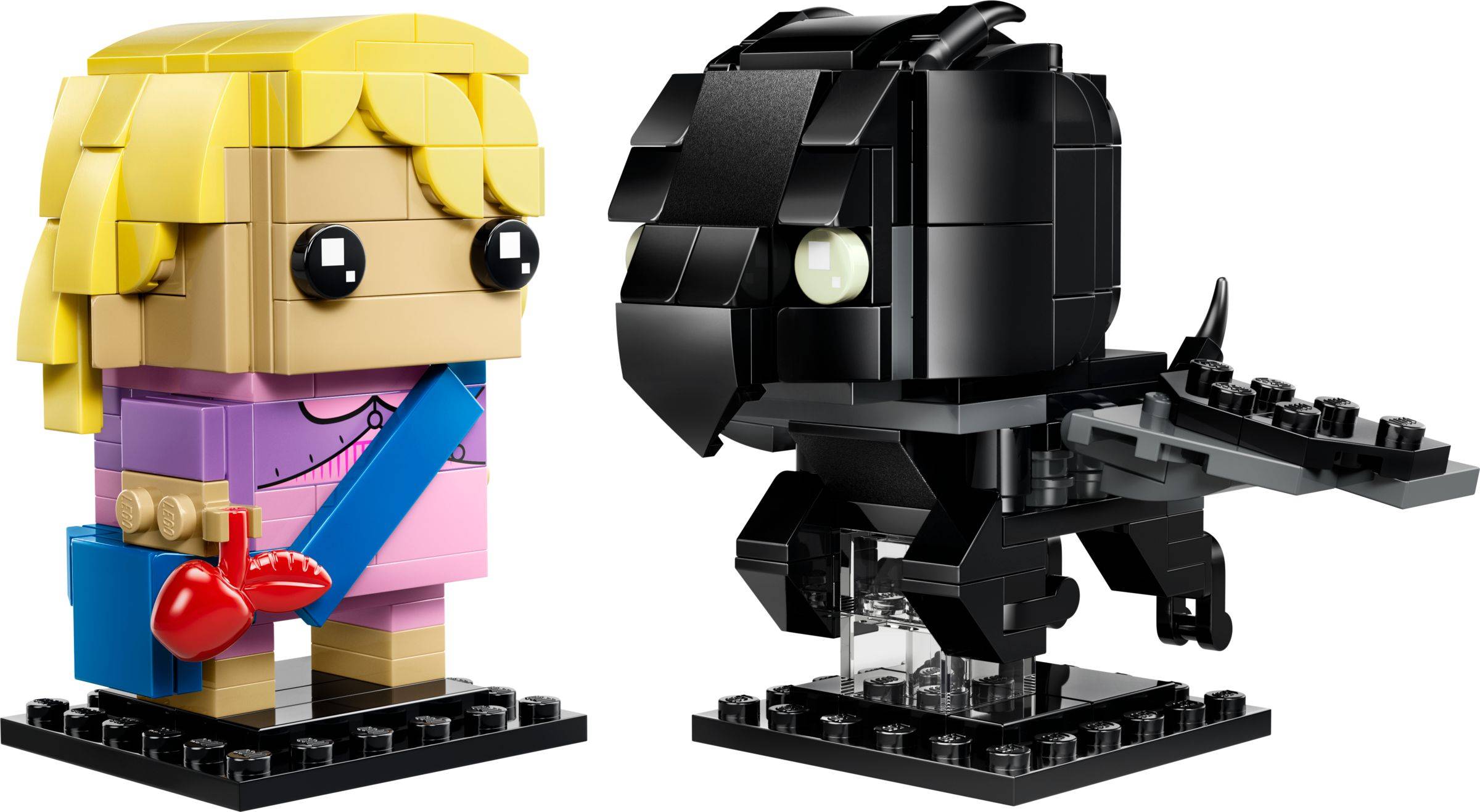 Zwei LEGO-ähnliche Ziegelfiguren auf schwarzen Ausstellungssockeln: ein blondes Mädchen in Rosa mit einem blauen Riemen und rotem Herz, neben einer schwarzen vogelähnlichen Figur, die eine Gitarre hält.