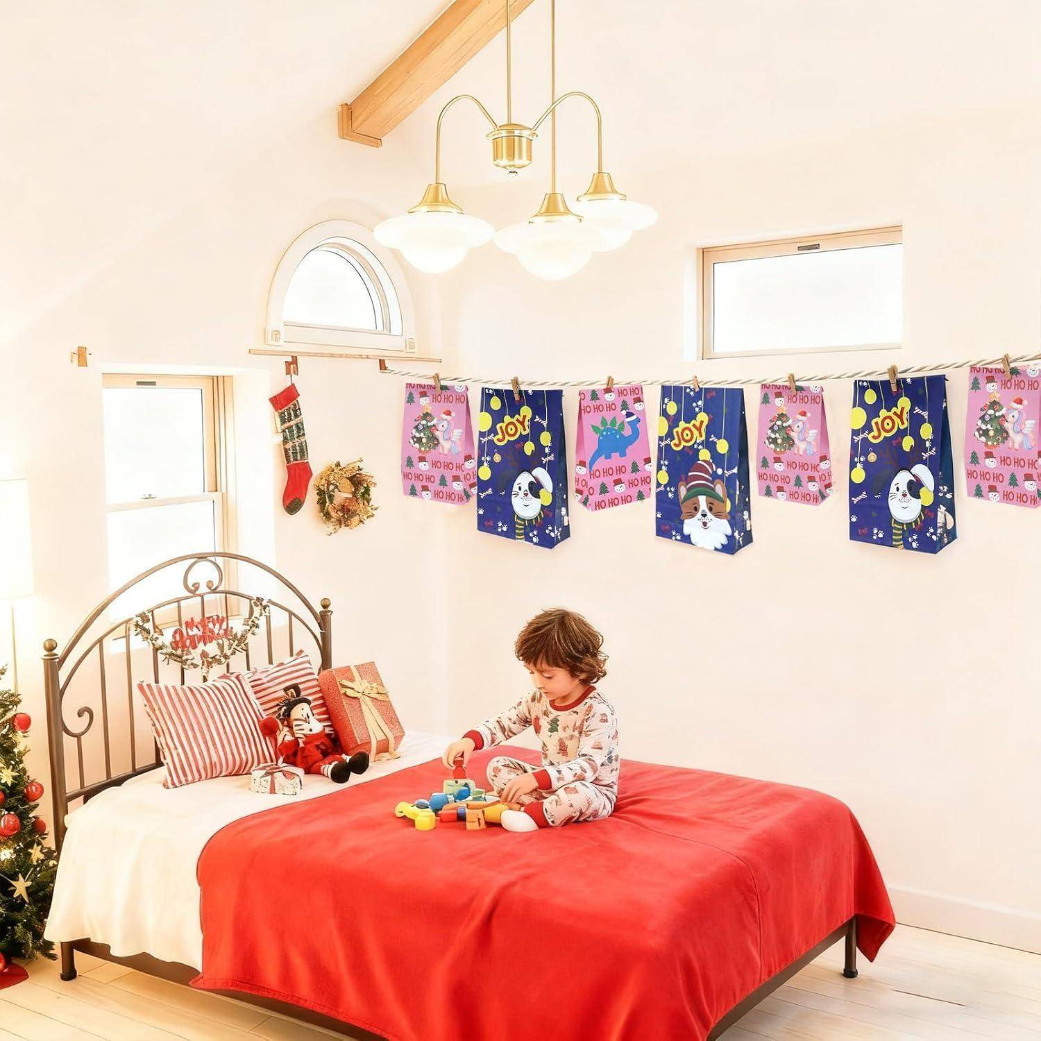 Kind im Schlafanzug, das mit Bausteinen auf einem roten Bett in einem hellen, festlich dekorierten Schlafzimmer mit Weihnachtsbannern und Strümpfen spielt.