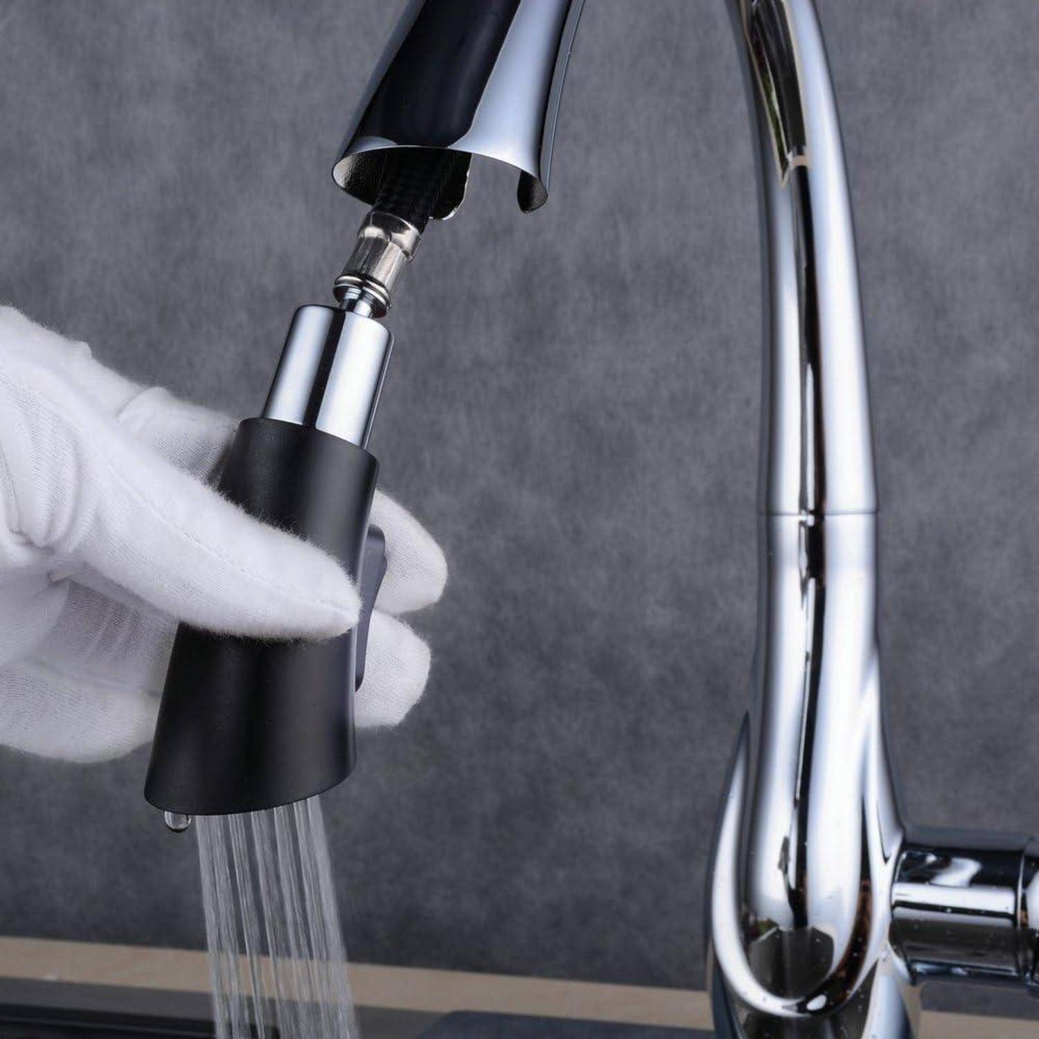 Mit Handschuh gehaltener abnehmbarer schwarzer Sprühkopf eines Wasserhahns mit sprühendem Wasser, angebracht an einem verchromten Küchenarmatur.
