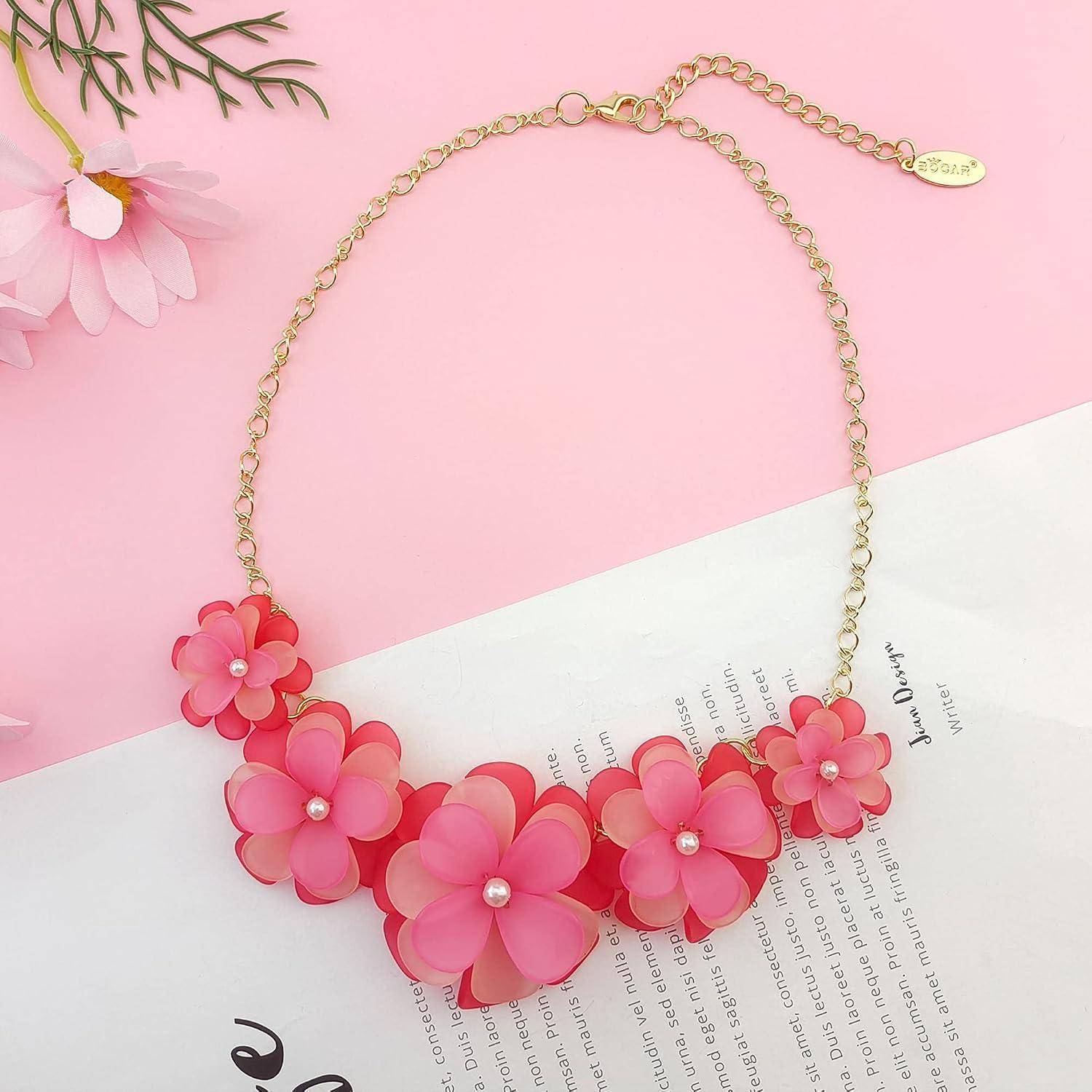 Goldkettenhals-Kette mit rosa Blütenanhänger-Clustern, gezeigt auf rosa-weißem Hintergrund.