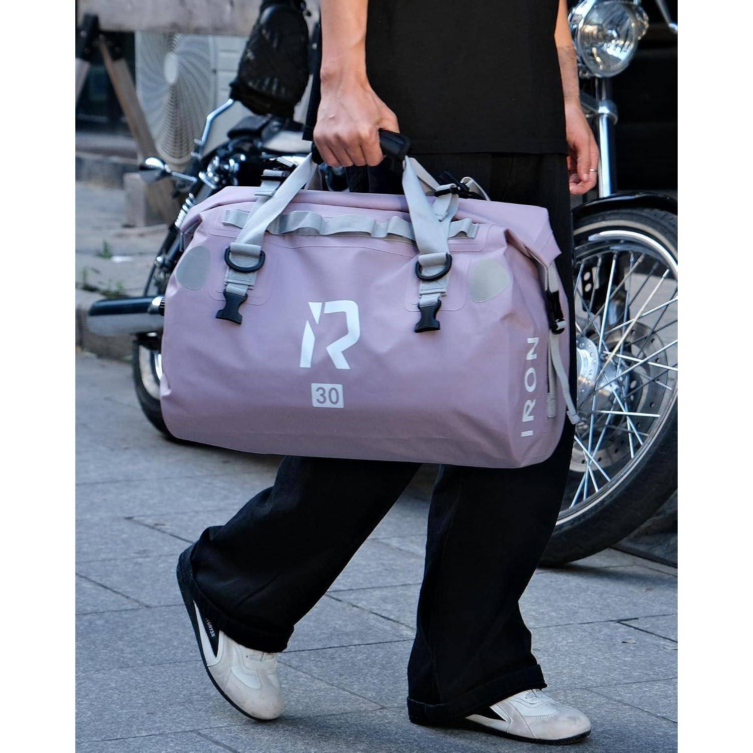 Eine Person trägt eine große lavendelfarbene Reisetasche mit der Aufschrift "IRON"" und ""30"" beim Gehen an geparkten Rollern vorbei.