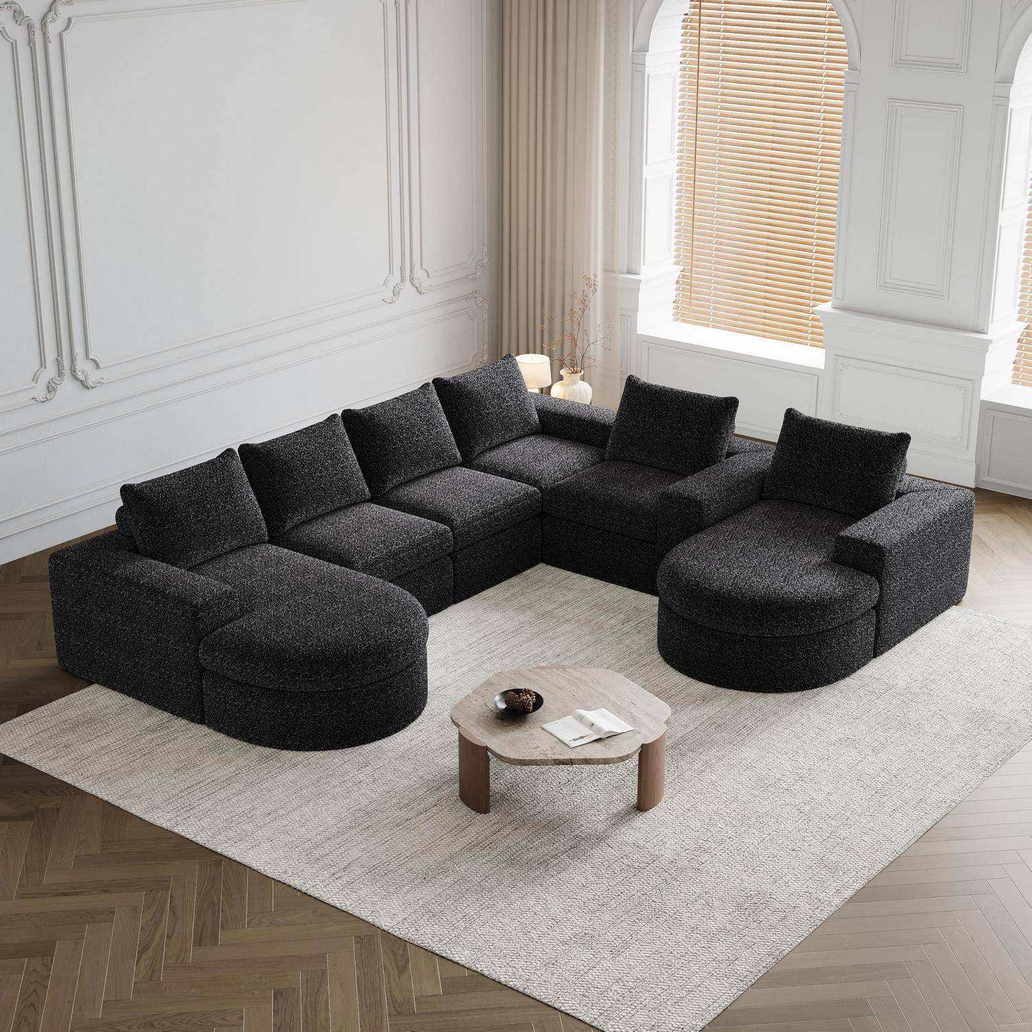 Dunkelgraues modulares Ecksofa in U-Form um einen hellen Holzcouchtisch auf einem großen beigefarbenen Teppich in einem hellen, minimalistischen Wohnzimmer angeordnet.