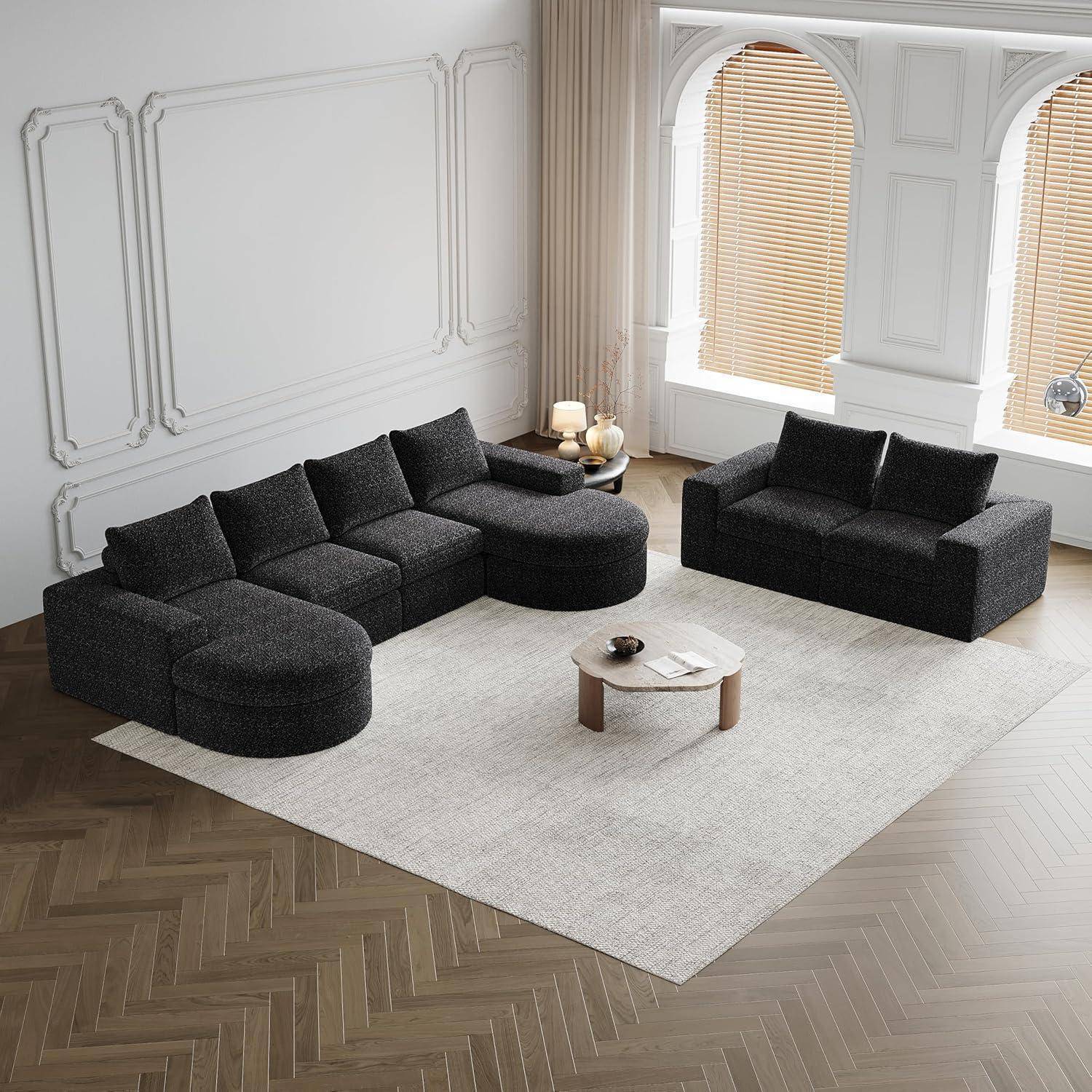Modernes Wohnzimmer mit einer dunklen modularen Eckgarnitur, passendem Loveseat, rundem Couchtisch und hellem Teppich neben hohen gewölbten Fenstern.
